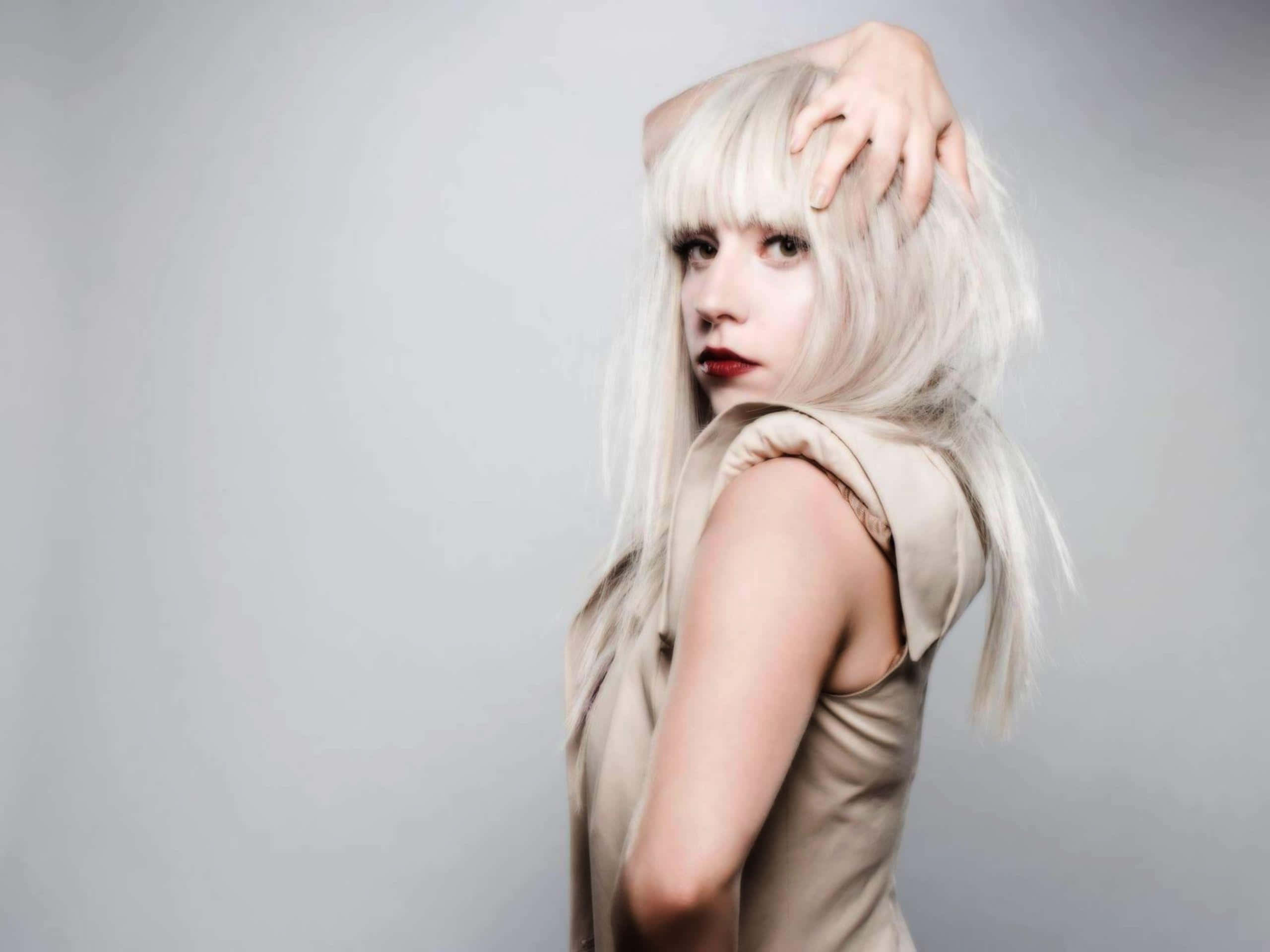 Lady Gaga 桌布 壁紙 — 一位擁有鉑金色頭髮和鮮豔紅唇的女性，在純灰色背景前擺姿勢，手放在頭上。