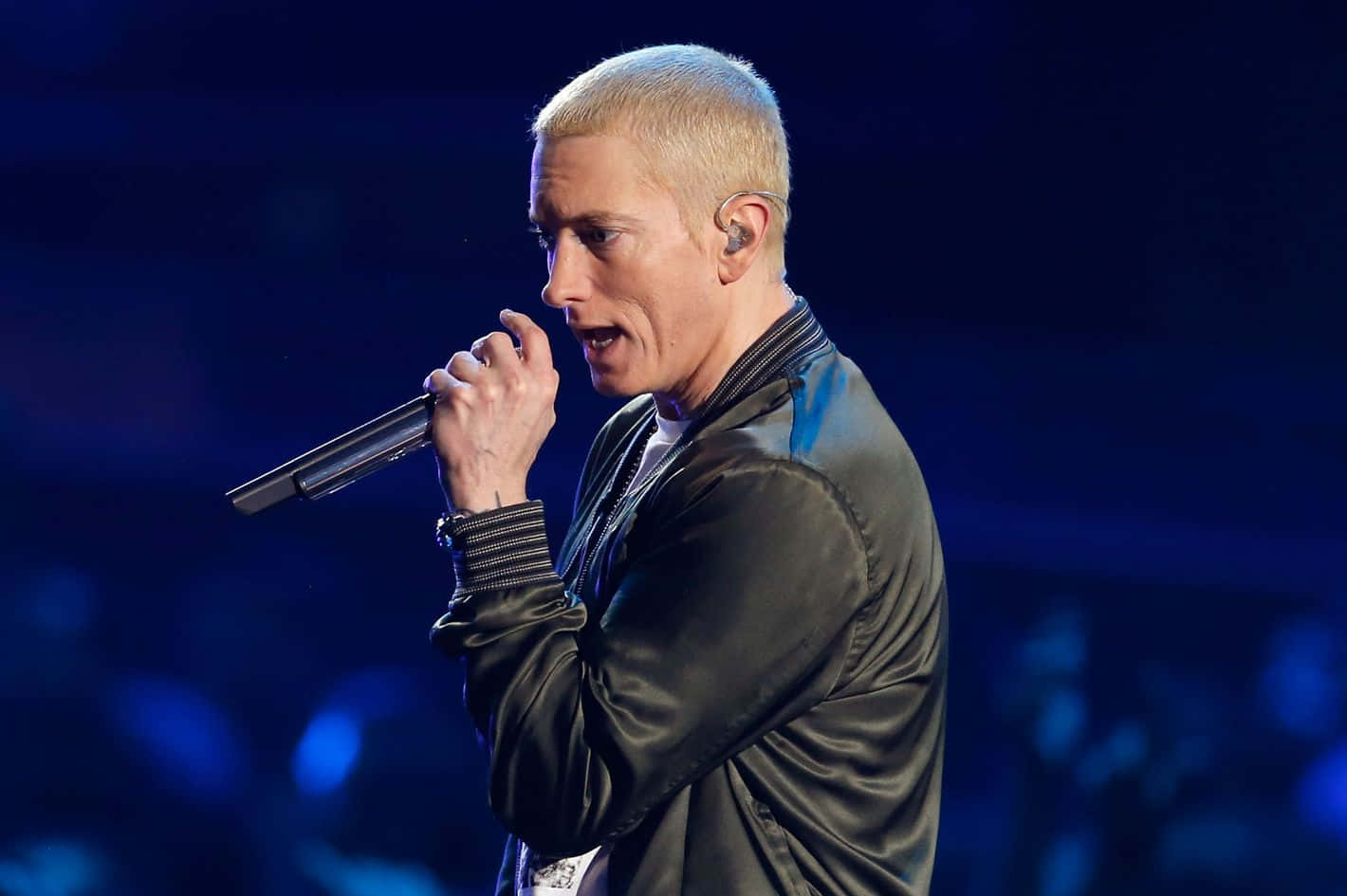 Eminem 桌布 壁紙 — 一位擁有鉑金色頭髮的男表演者在深藍色舞台燈光下，熱情地對著麥克風唱歌。