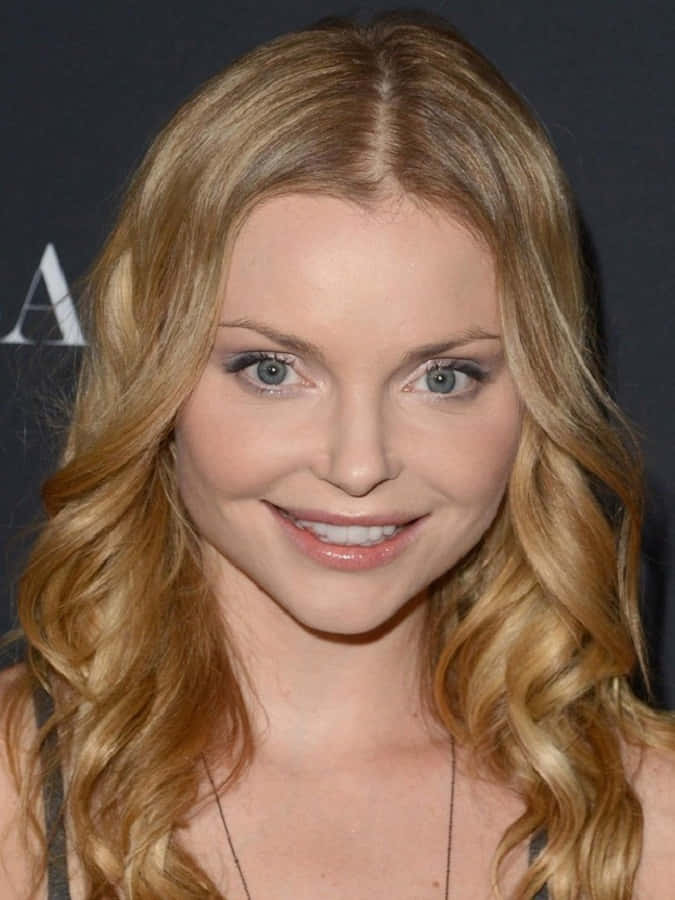 Izabella Miko 桌布 壁紙 — 一位擁有長波浪金髮和明亮藍眼睛的女性，對著鏡頭溫暖微笑的特寫肖像。