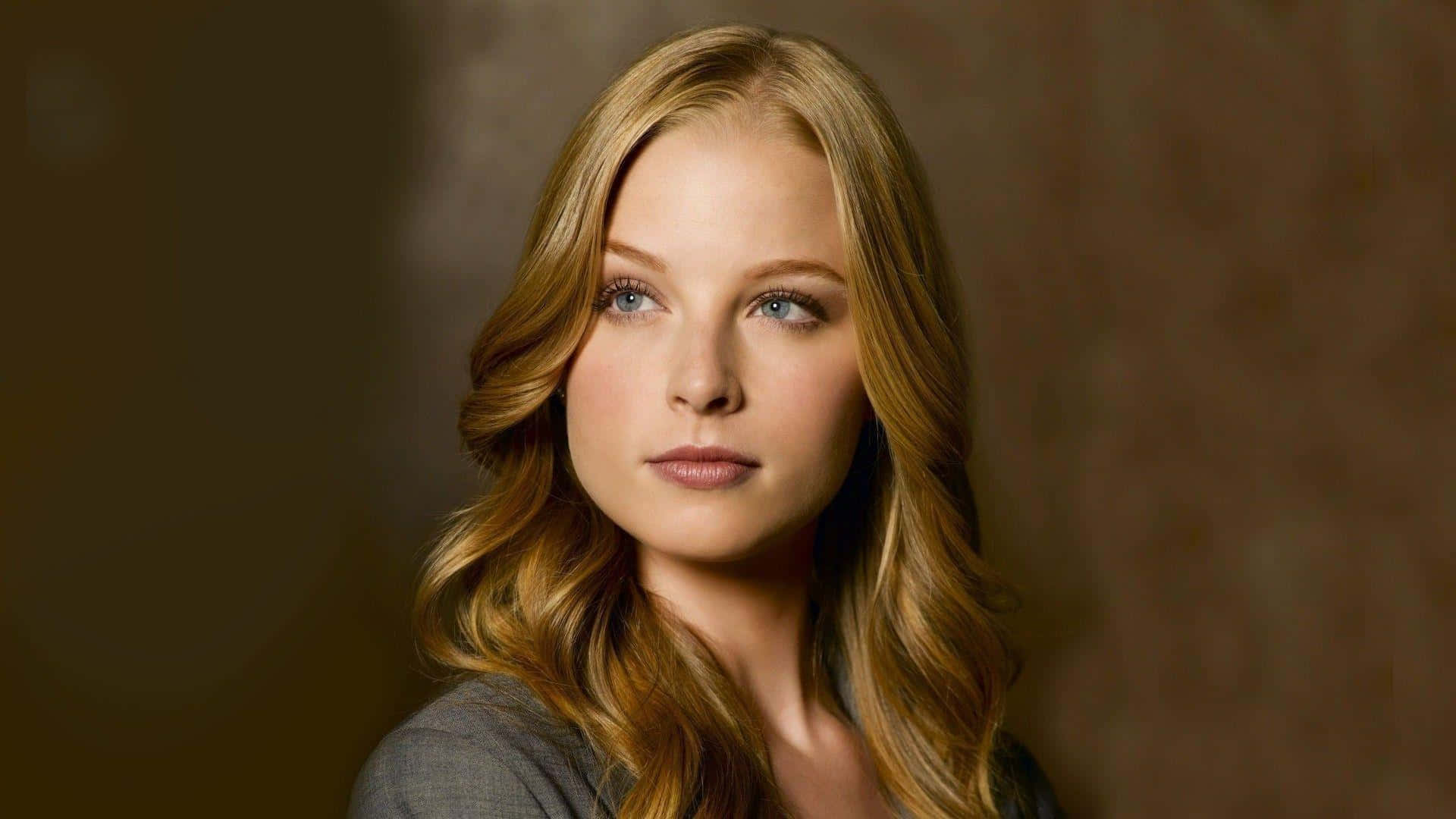 rachel nichols 桌布 壁紙 — 一位擁有長波浪金髮和藍眼睛的女性，在溫暖的棕色紋理背景前溫柔凝視。