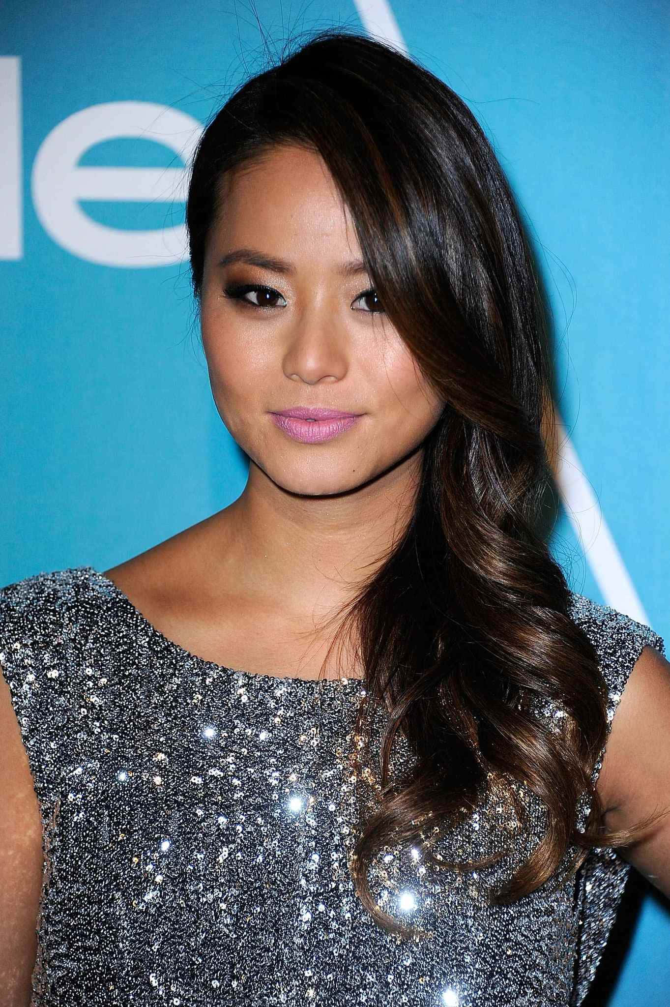 Jamie Chung 桌布 壁紙 — 一位擁有長深色波浪髮的女性，在帶有白色文字的藍色背景前穿著閃亮的銀色連衣裙。