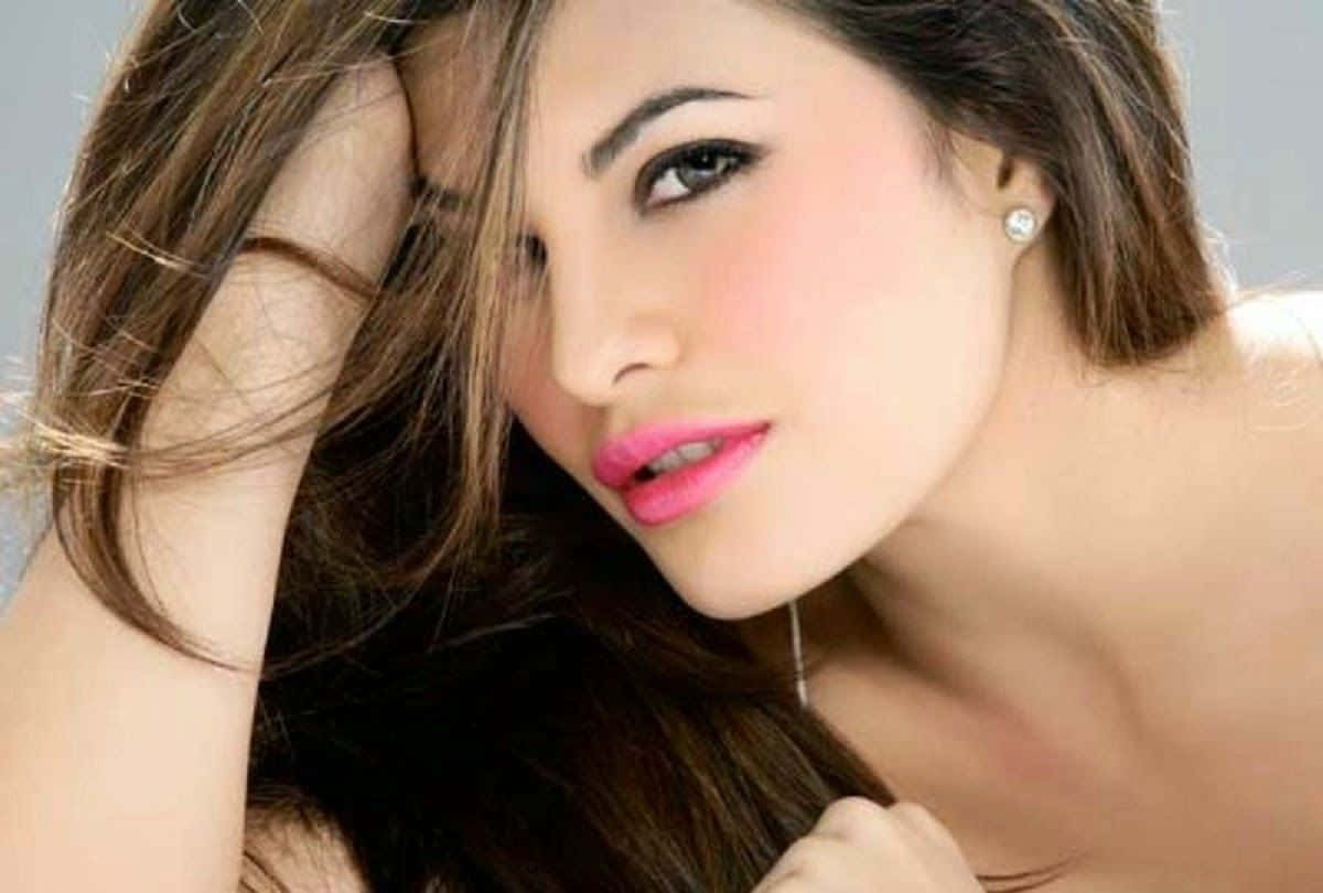 Jacqueline Fernandez 桌布 壁紙 — 一位擁有長長棕色頭髮和亮粉色唇膏的女性，將頭靠在手上，直視鏡頭。
