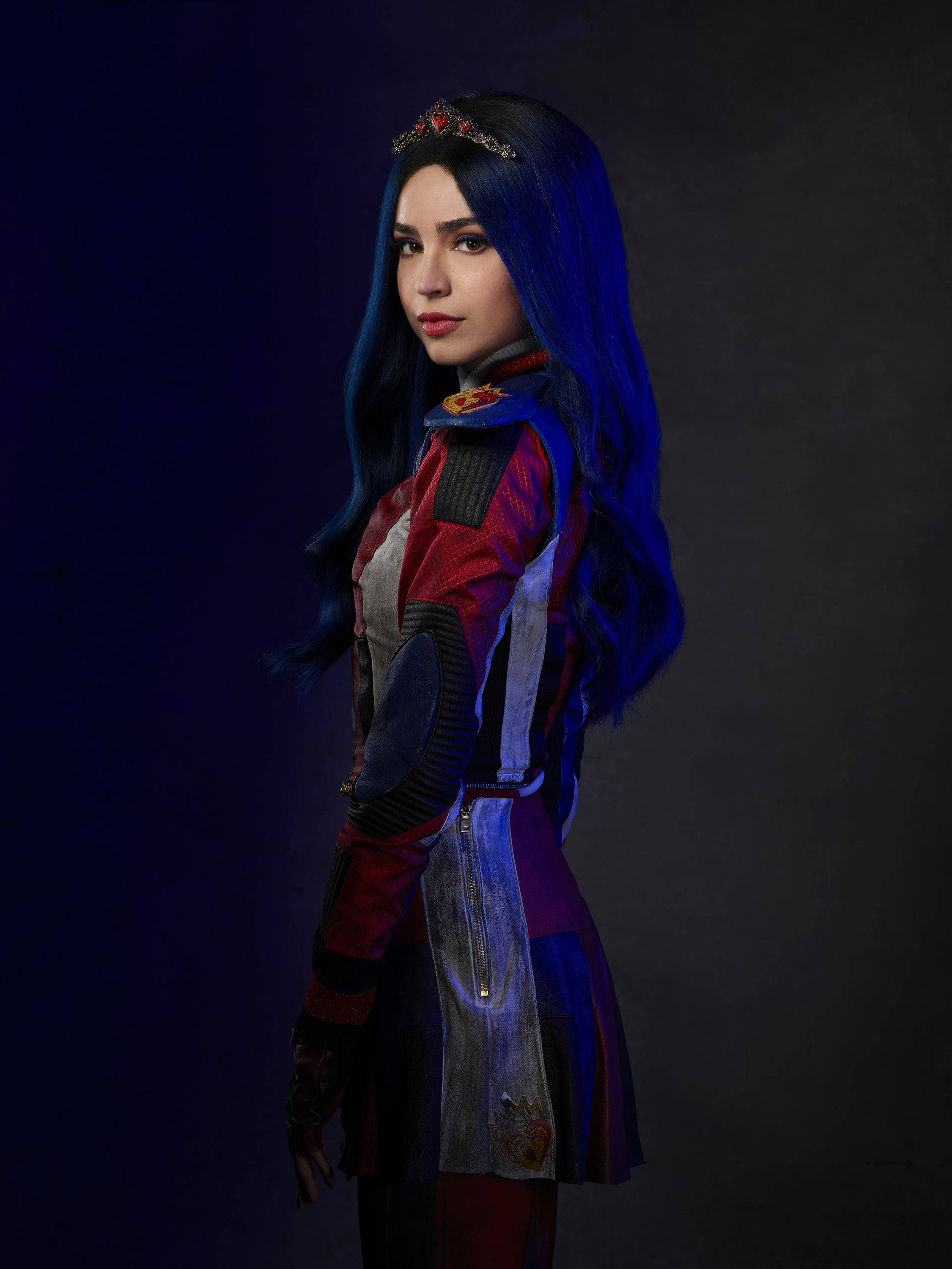 Descendants 桌布 壁紙 — 一位擁有長長藍色頭髮和鑲有寶石皇冠的女性，在深色背景下穿著紅色、紫色和銀色的未來風格服裝。