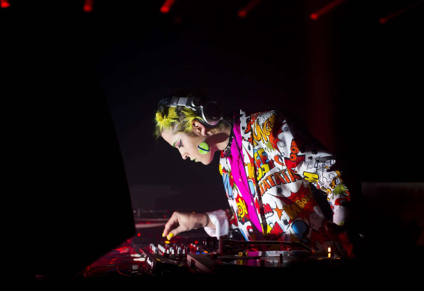 DJ 桌布 壁紙 — 一位擁有霓虹髮色和漫畫風格外套的DJ，在黑暗的俱樂部中於紅色舞台燈光下混音。
