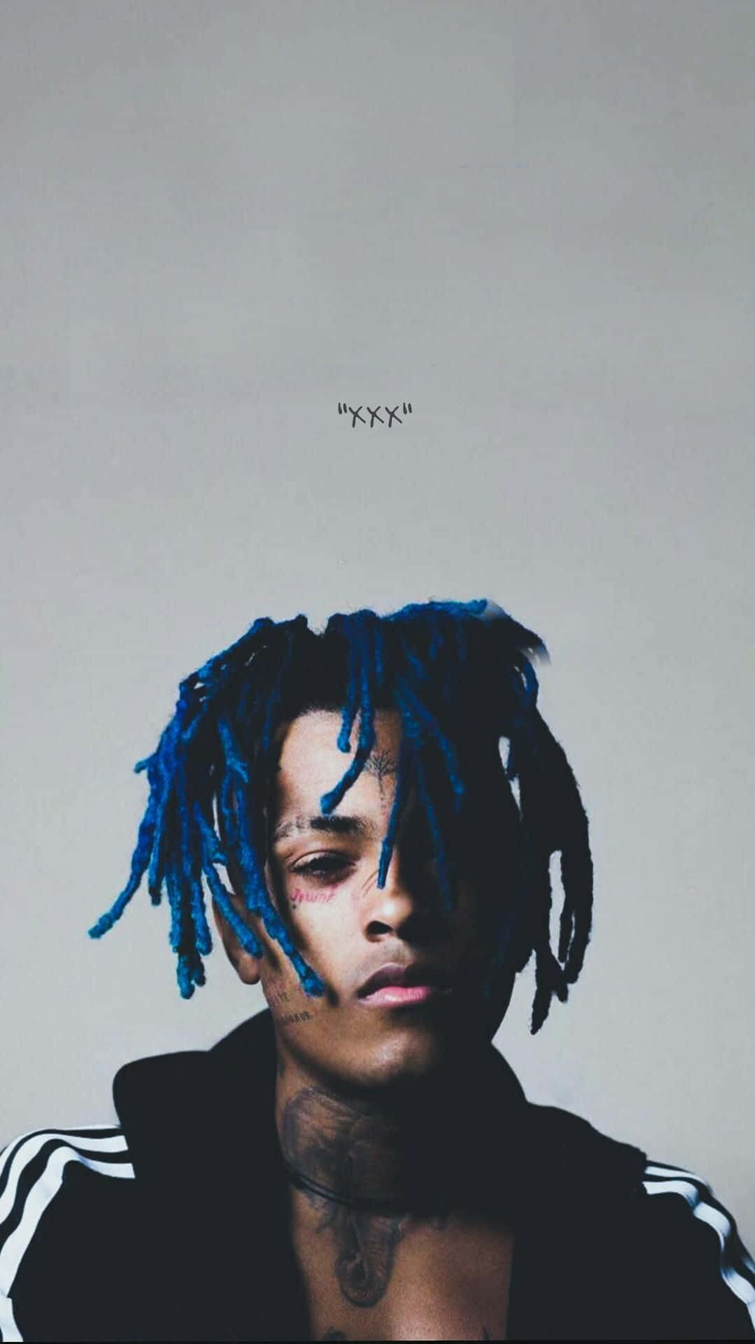 Dead Rappers Blue 壁紙 — 一位擁有鮮艷藍色辮子頭和紋身的男士肖像，背景為純灰色。