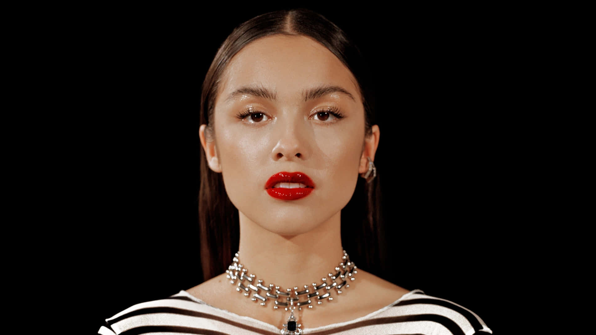 Olivia Rodrigo 桌布 壁紙 — 一位擁有鮮豔紅唇和銀飾的女性，在純黑背景下強烈凝視。