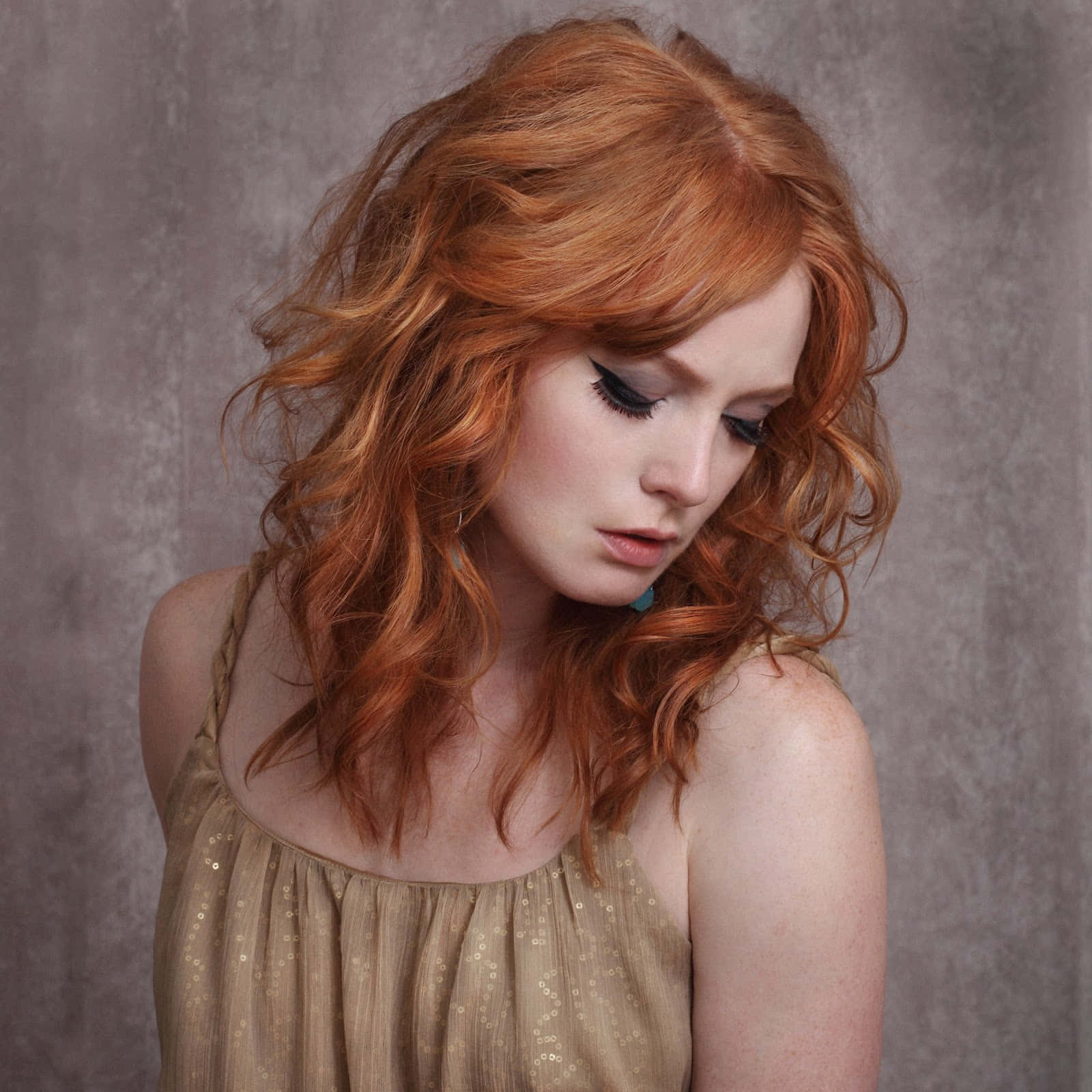 Alicia Witt 桌布 壁紙 — 一位擁有鮮豔紅色波浪長髮和深色眼線的女性，在柔和的灰色紋理背景前向下凝視。