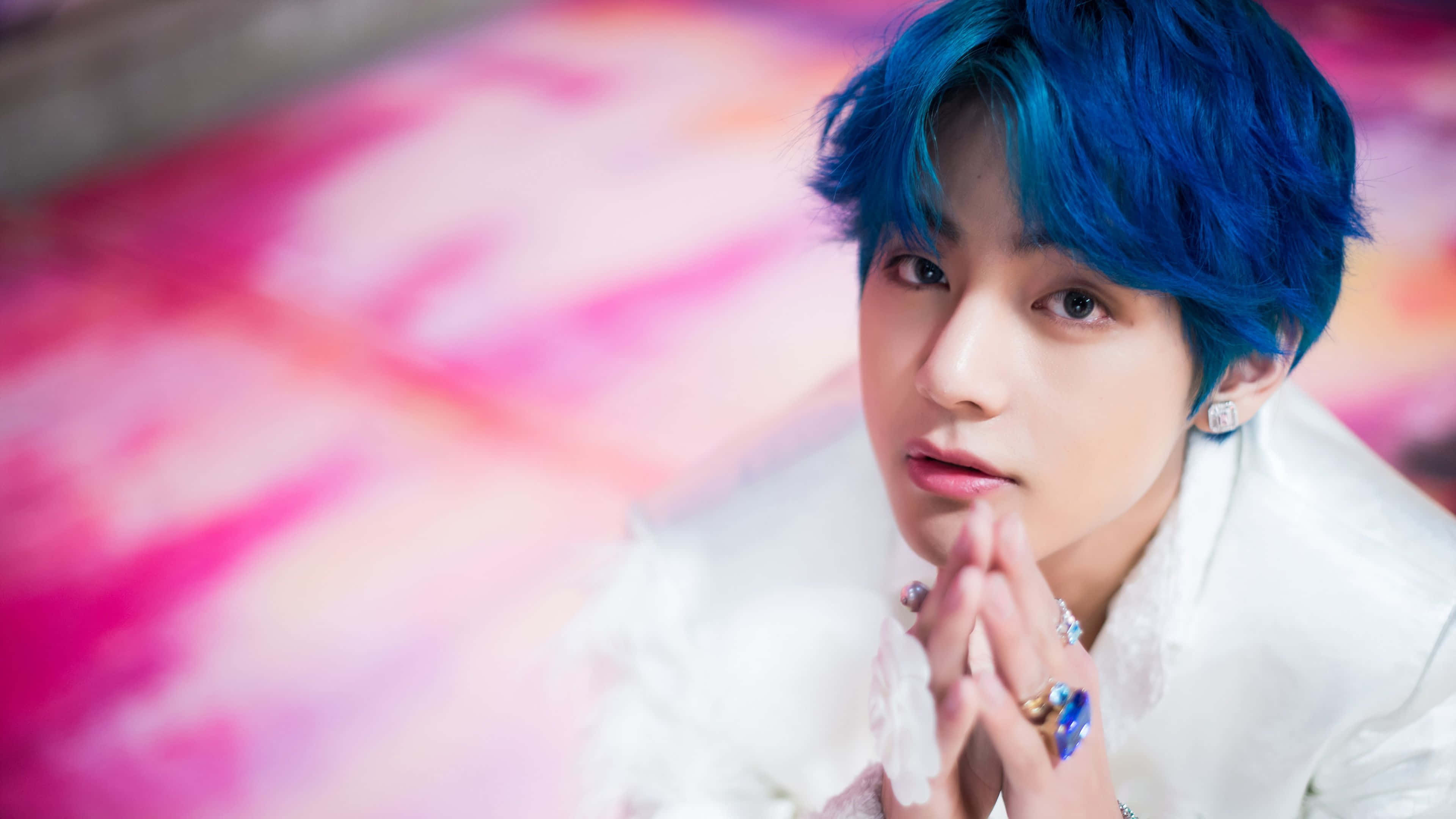 Taehyung Cute 桌布 壁紙 — 一位擁有鮮豔藍色頭髮和白色服裝的年輕男子，在夢幻般的粉紅色和橙色模糊背景前溫柔地凝視。