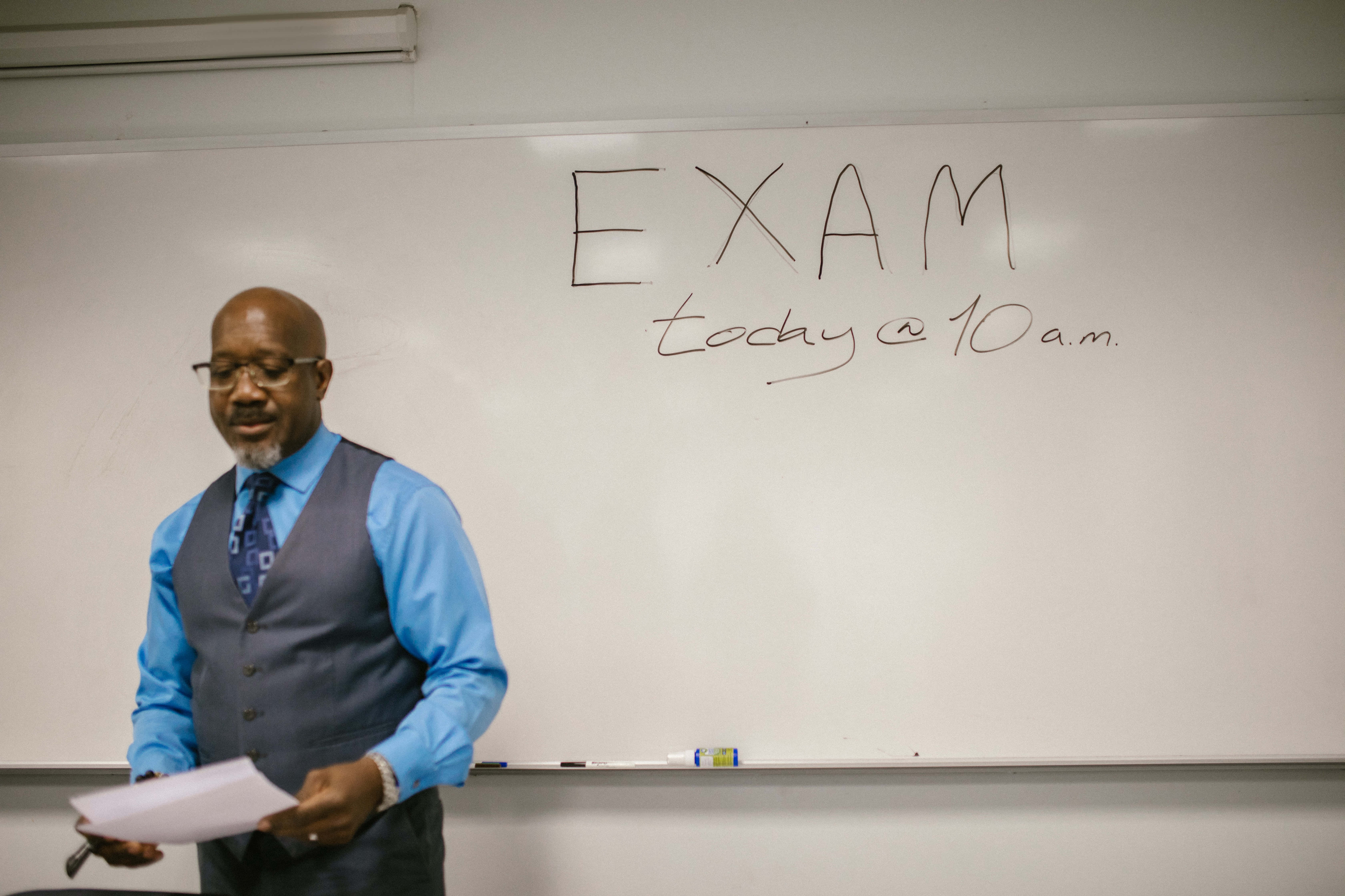 Teacher 桌布 壁紙 — 一位教授站在白板前，表情嚴肅地宣布上午10點有考試。