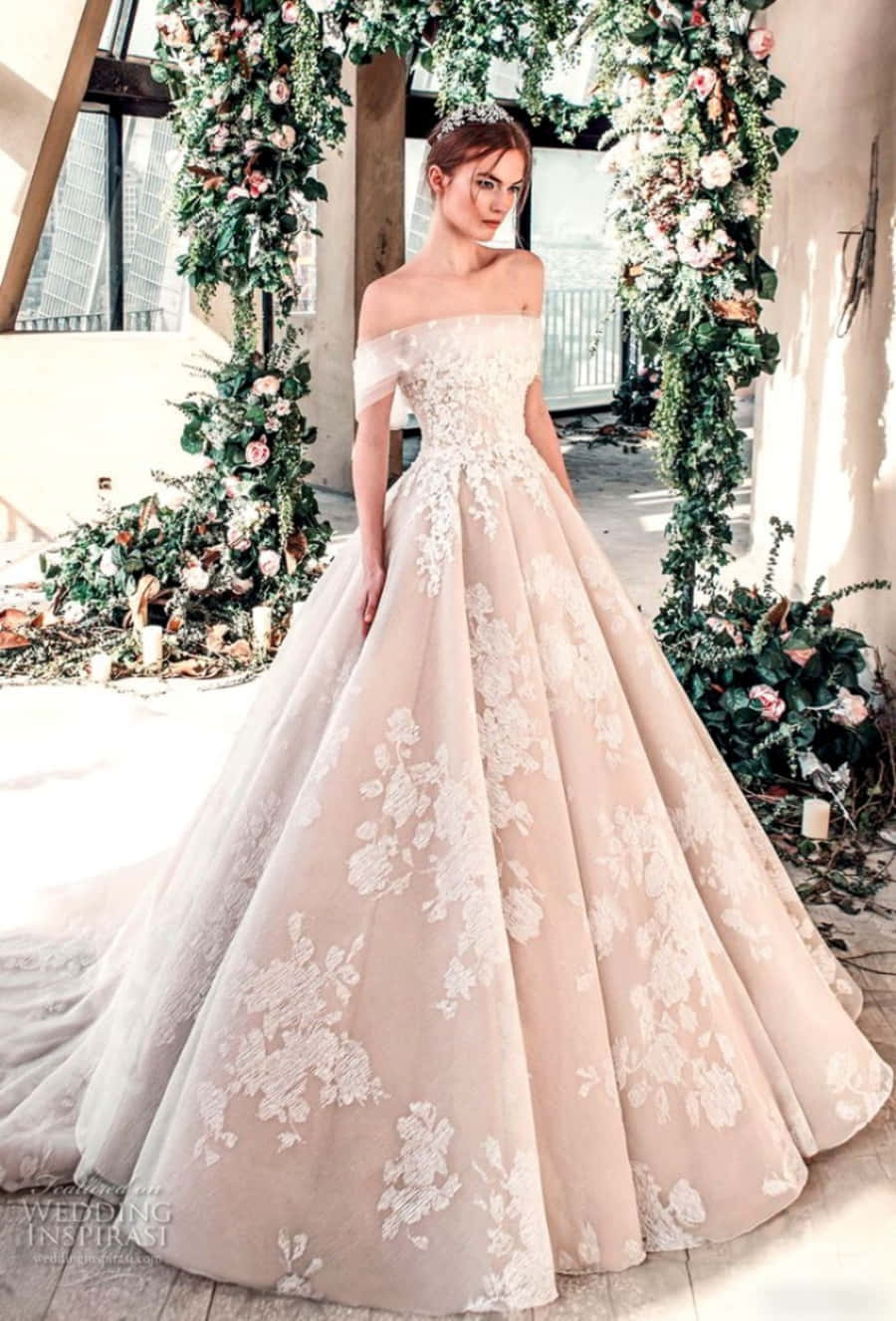 Wedding Dress 桌布 壁紙 — 一位新娘穿著淡粉紅色露肩婚紗，帶有白色花卉刺繡，站在茂盛的綠色和粉紅色花卉拱門下。