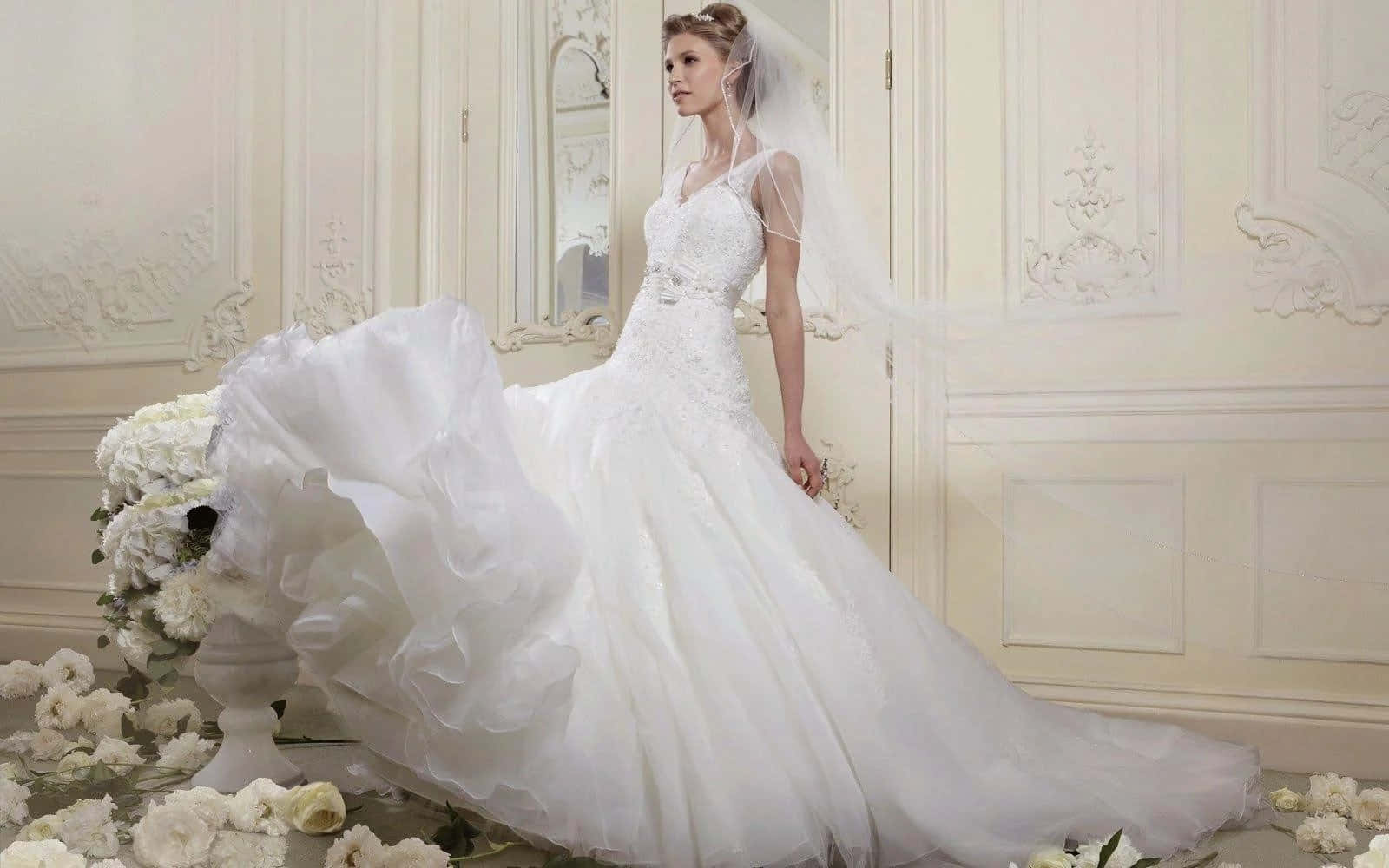 Wedding Dress 桌布 壁紙 — 一位新娘穿著華麗的白色婚紗，披著飄逸的頭紗，站在一個裝飾華麗的房間裡的花藝佈置旁邊。