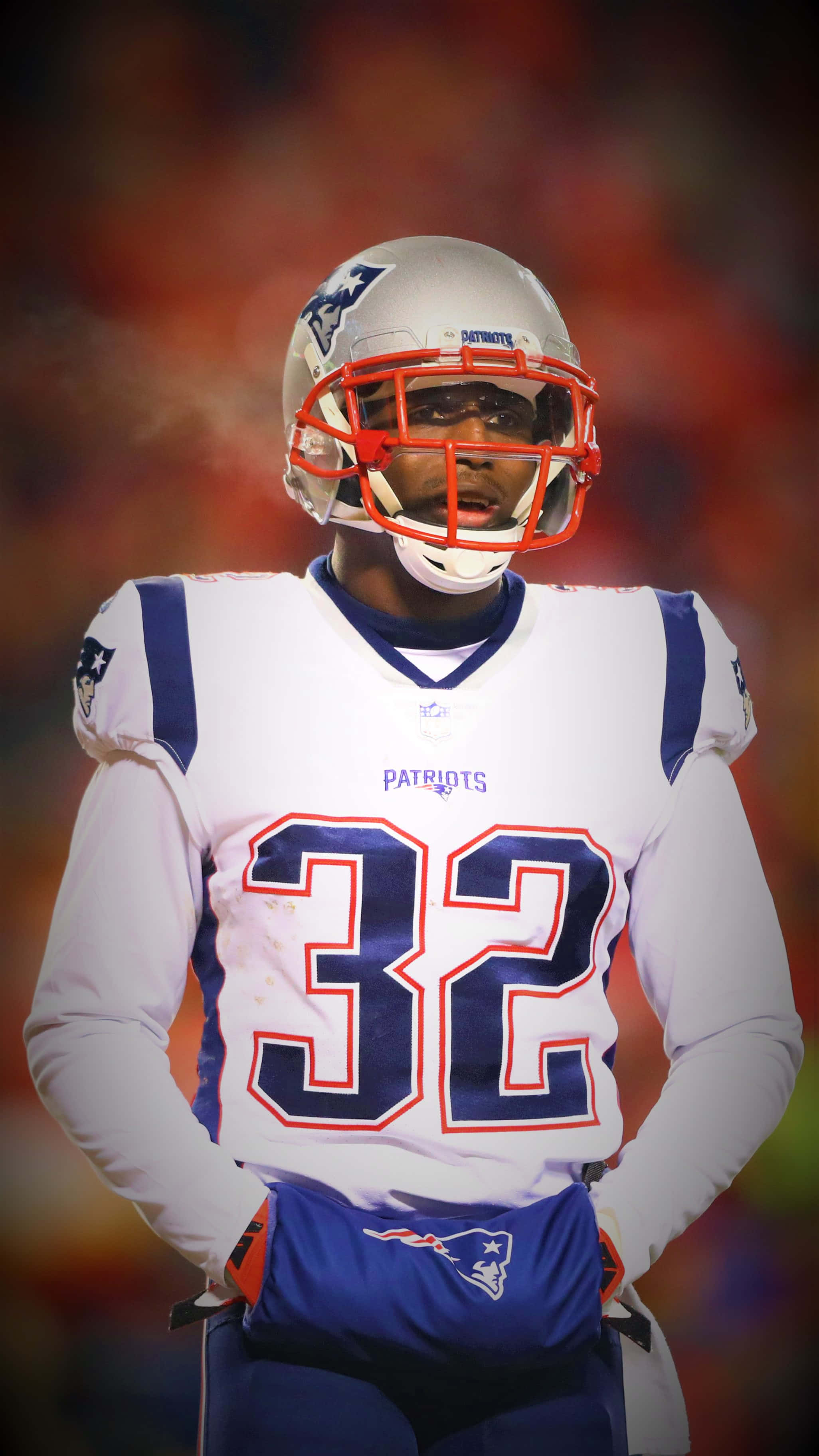 Devin Mccourty 桌布 壁紙 — 一位新英格蘭愛國者隊美式足球員身穿32號球衣，在球場燈光下專注站立，背景是模糊的人群。