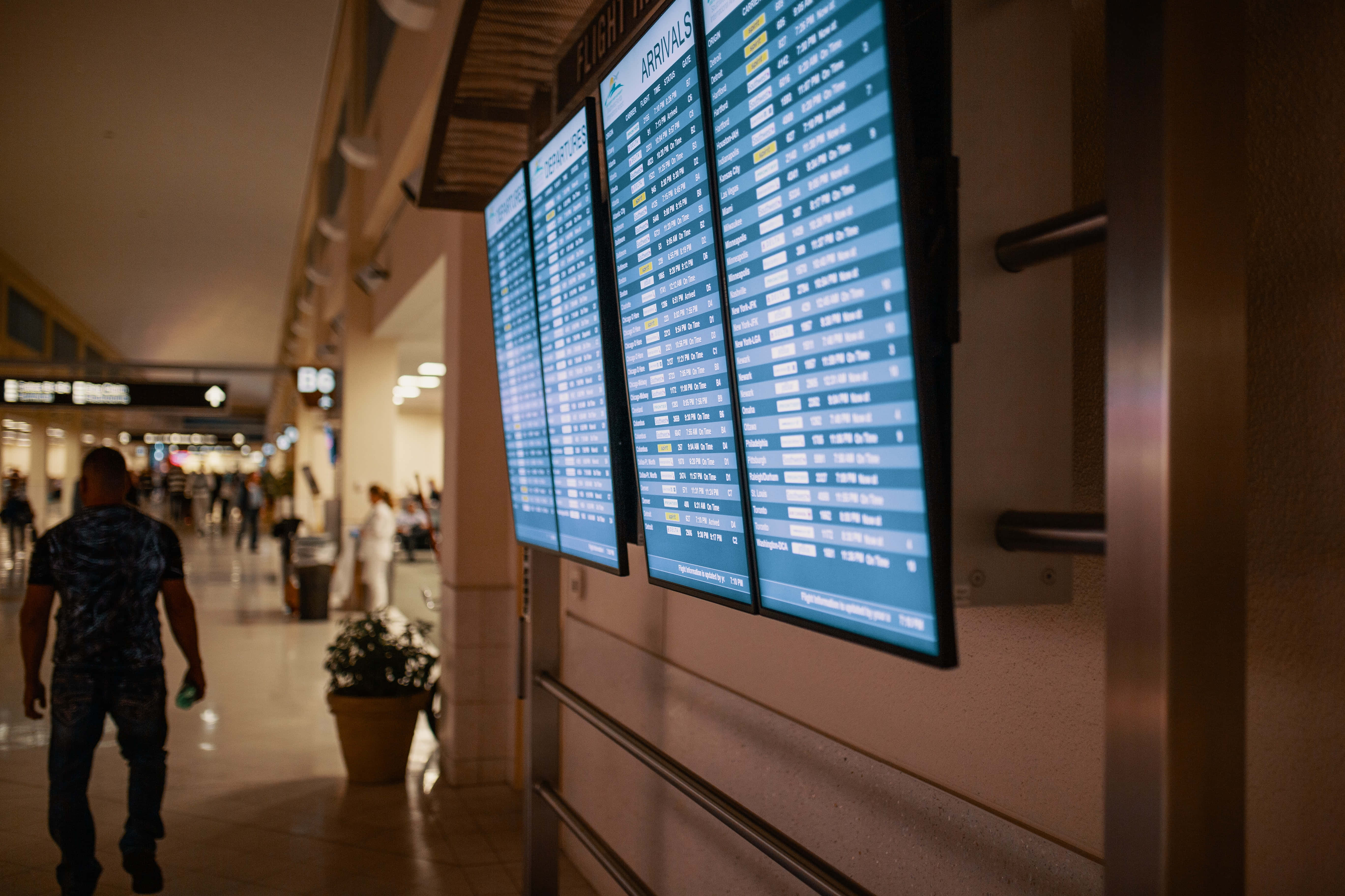 Airport 桌布 壁紙 — 一位旅客走過昏暗機場客運大樓走廊中發光的數碼航班到達顯示板。
