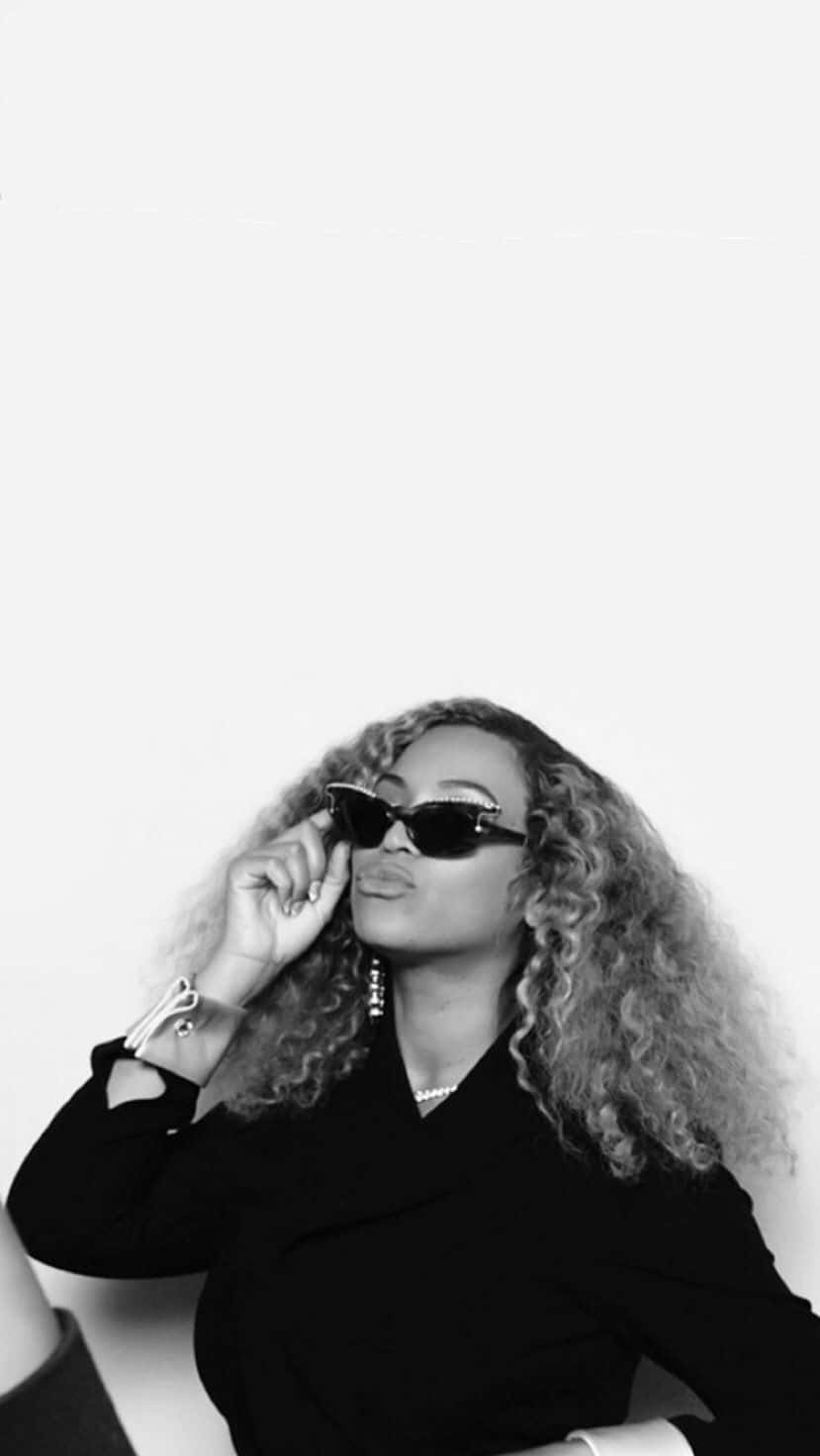 Beyoncé 桌布 壁紙 — 一位時尚女性，擁有豐盈的捲髮和太陽眼鏡，在純白背景前自信地擺出黑白造型。