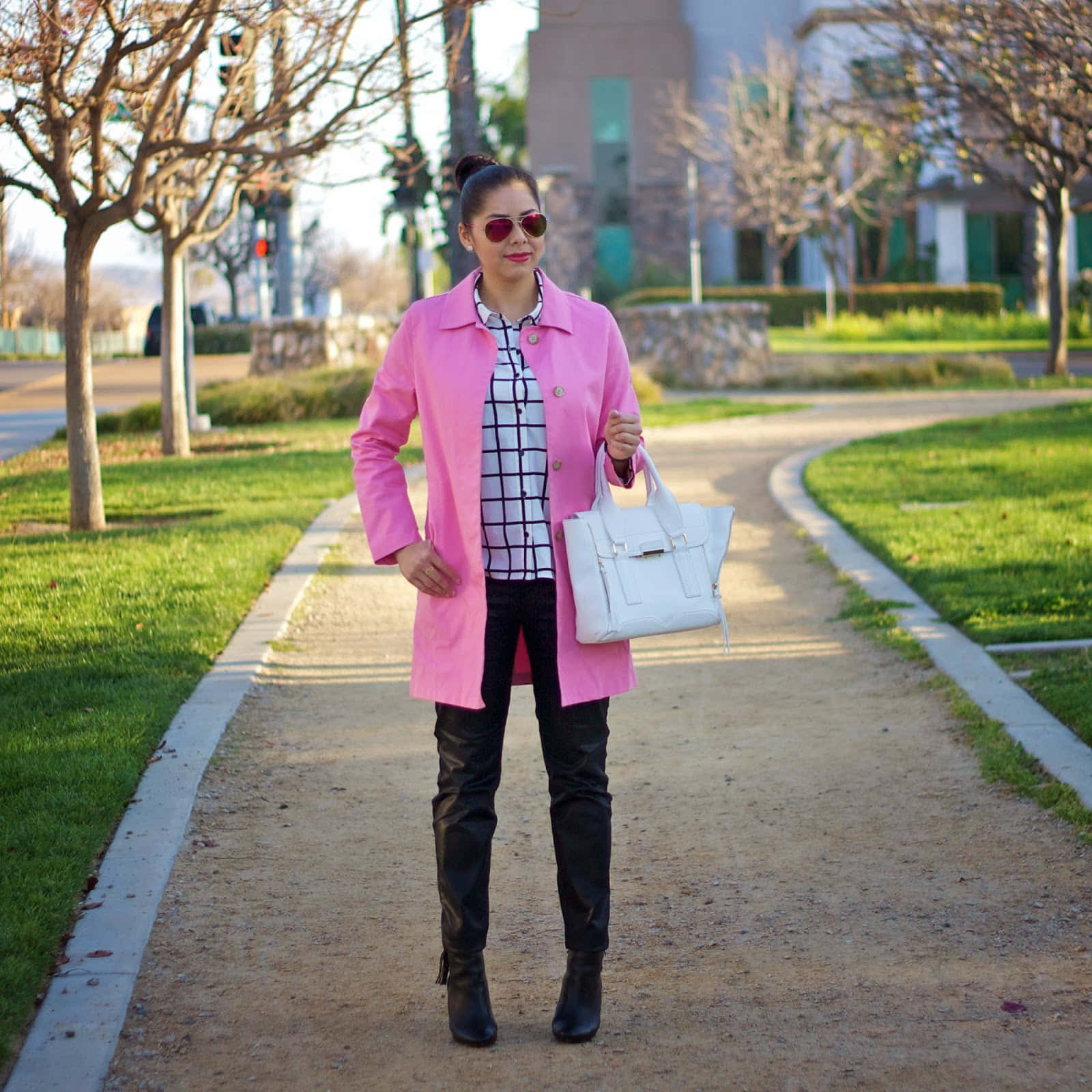 Pink Coat 桌布 壁紙 — 一位時尚女性穿著亮粉色外套和太陽眼鏡，自信地走在陽光明媚的公園小徑上。