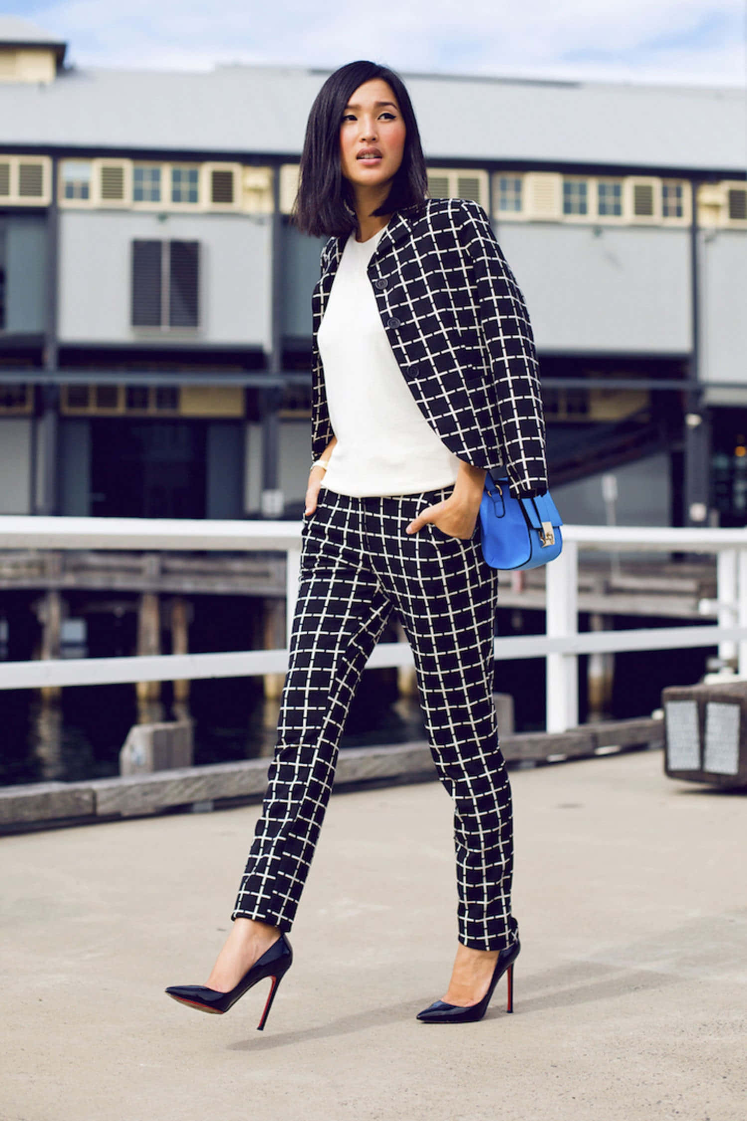 Black And White Fashion 桌布 壁紙 — 一位時尚女性身穿黑白格紋西裝，自信地站在海濱碼頭，手持藍色手袋。
