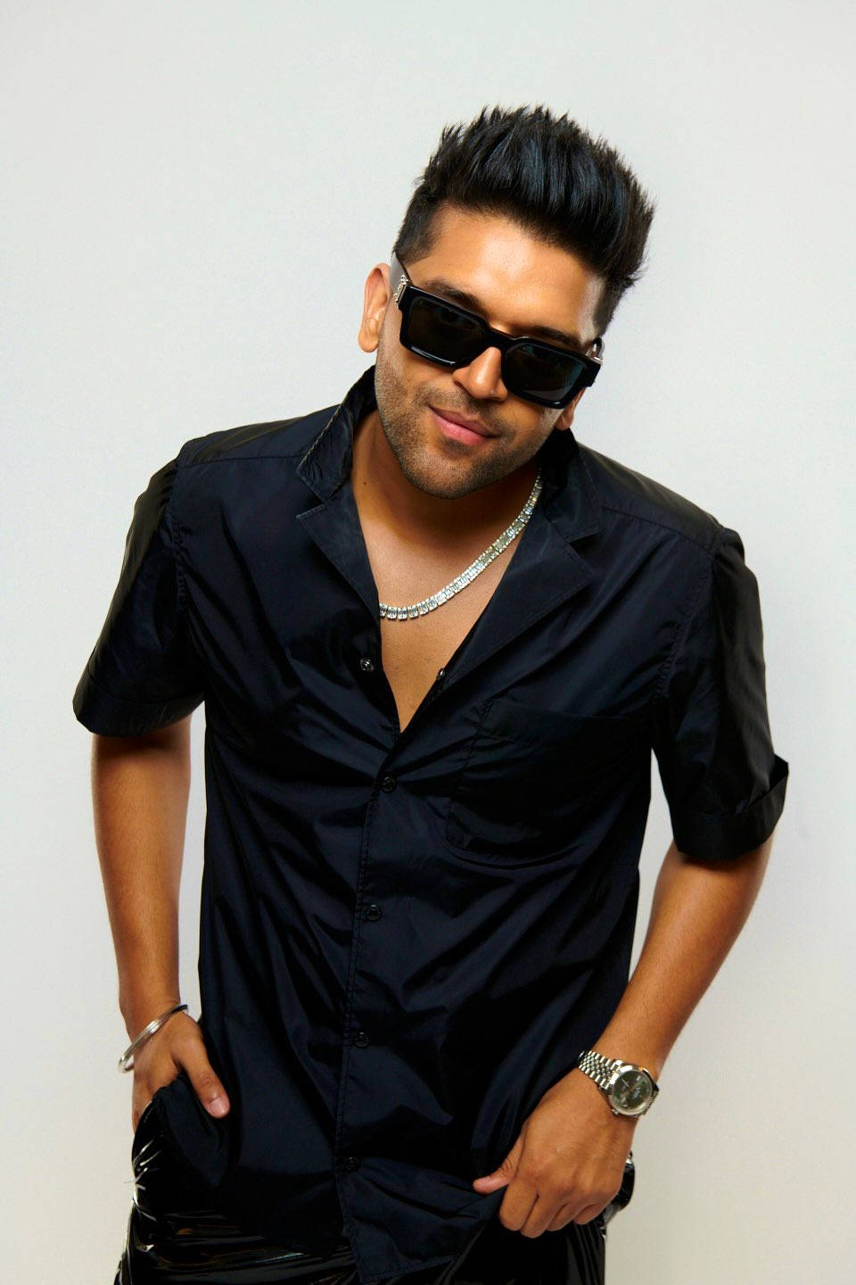 Guru Randhawa 桌布 壁紙 — 一位時尚男士戴著黑色太陽眼鏡和閃亮襯衫，在純白背景前自信地擺姿勢。