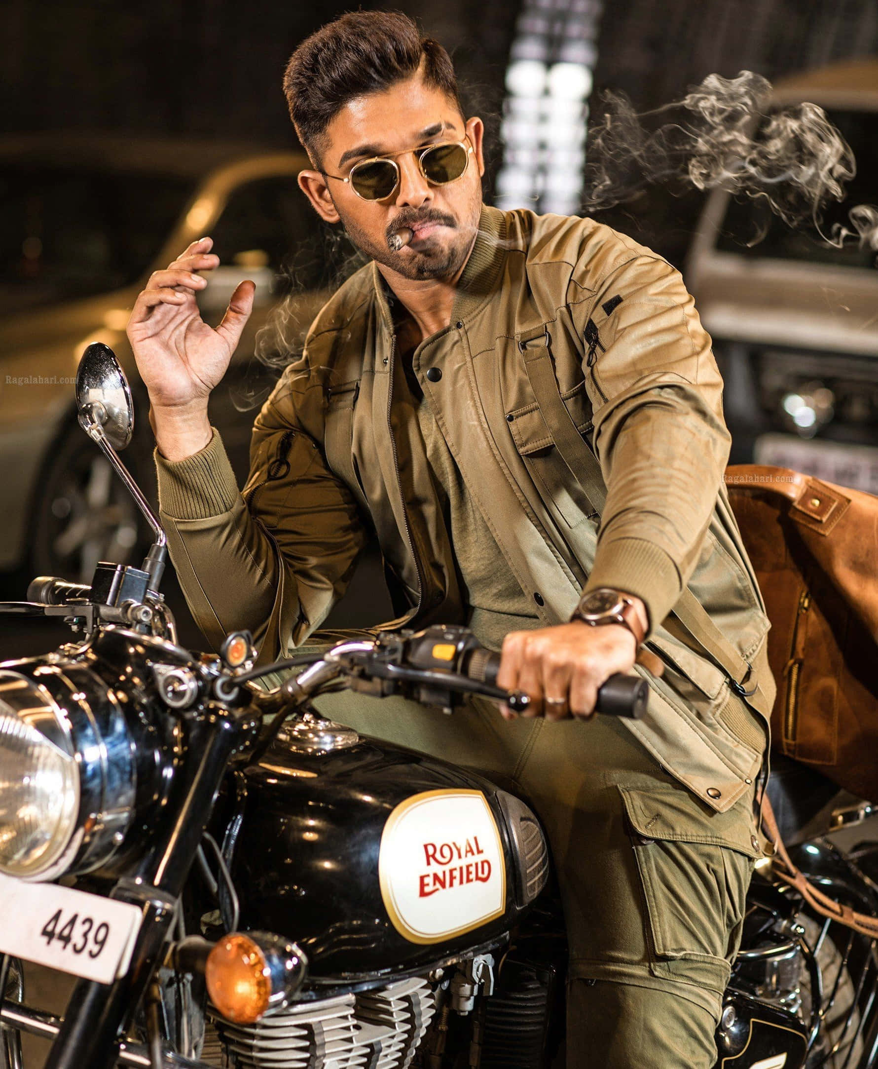 Allu Arjun 桌布 壁紙 — 一位時尚男士穿著棕褐色外套和太陽眼鏡，晚上坐在黑色Royal Enfield電單車上抽煙。