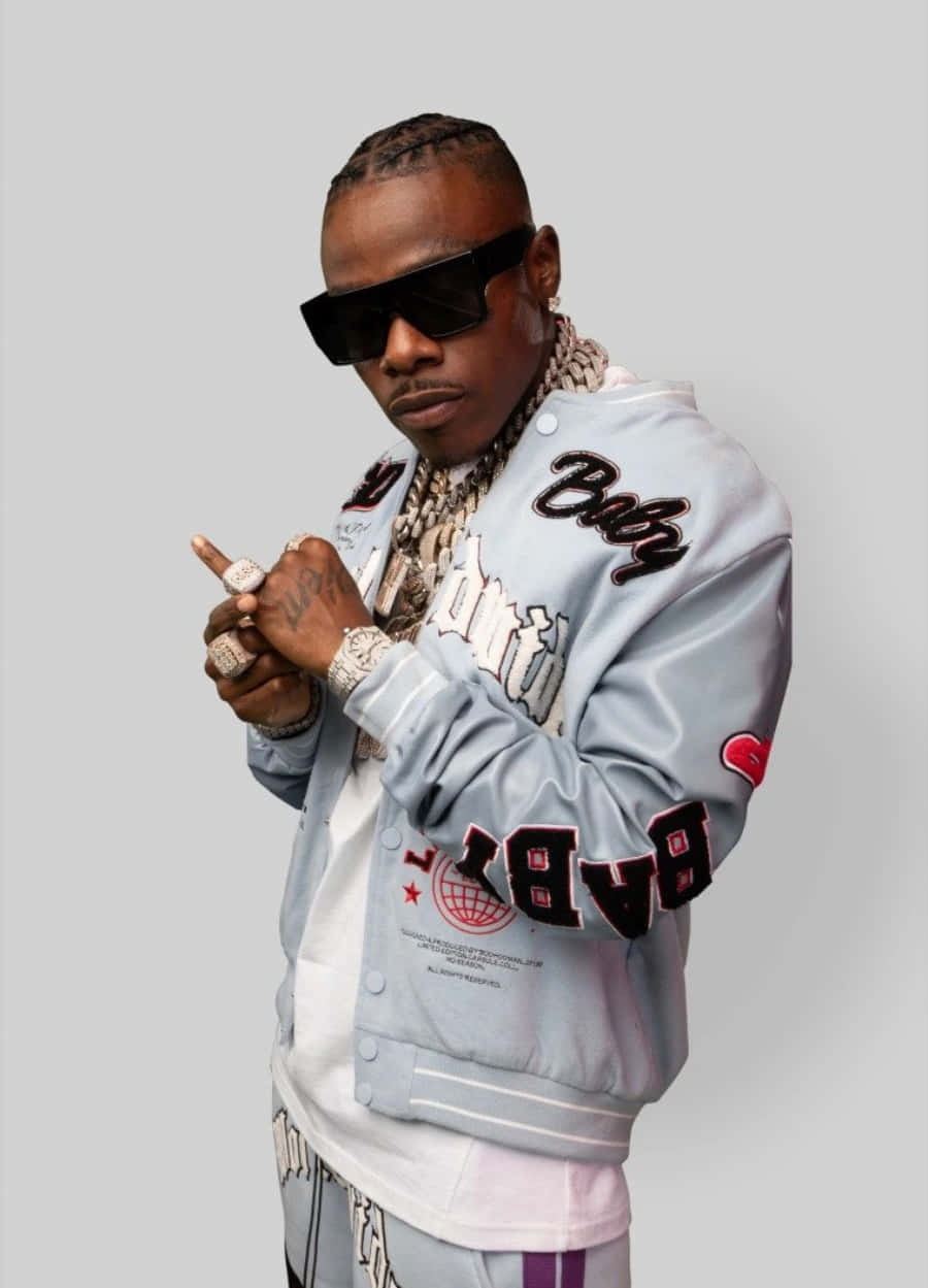 Dababy 桌布 壁紙 — 一位時尚男士身穿淺灰色大學外套，帶有醒目字母和鏈條，在純灰色背景前自信地擺姿勢。