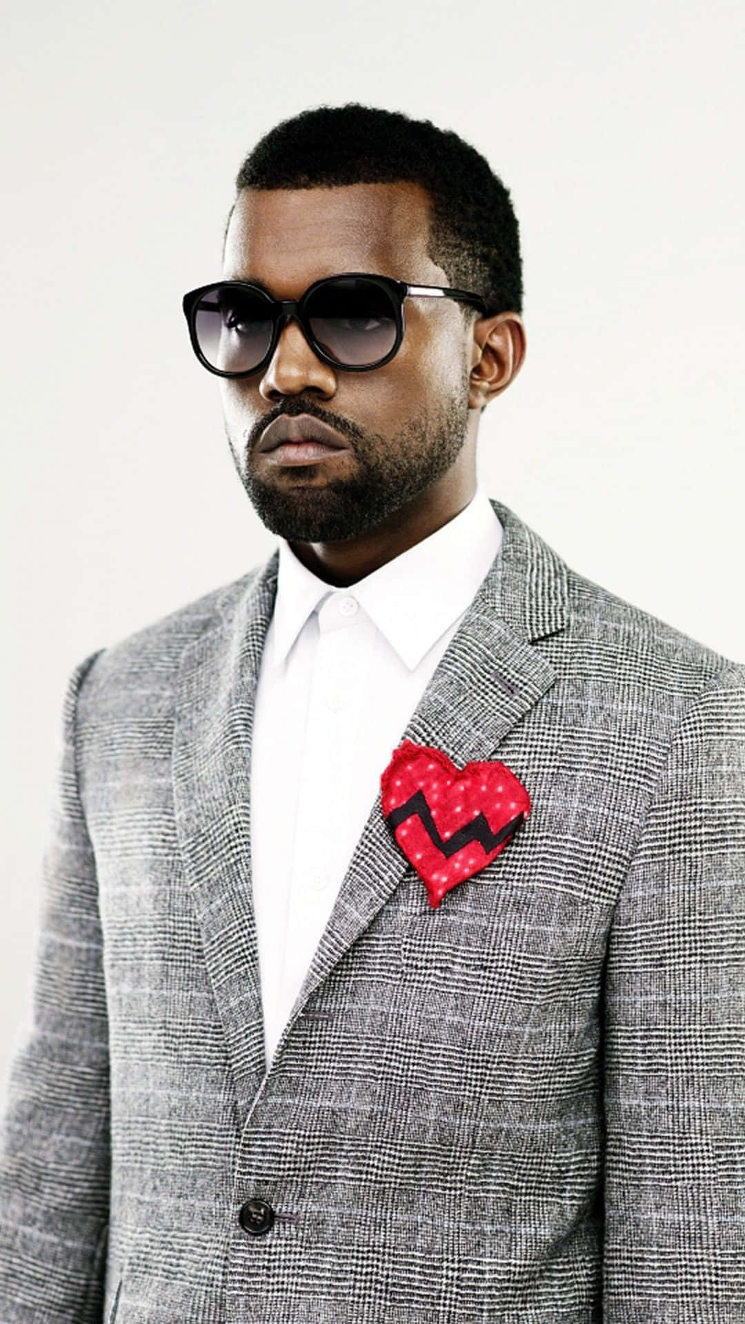 Kanye 桌布 壁紙 — 一位時尚男士身穿灰色格紋西裝和太陽眼鏡，在純白背景前佩戴紅色心形口袋方巾。