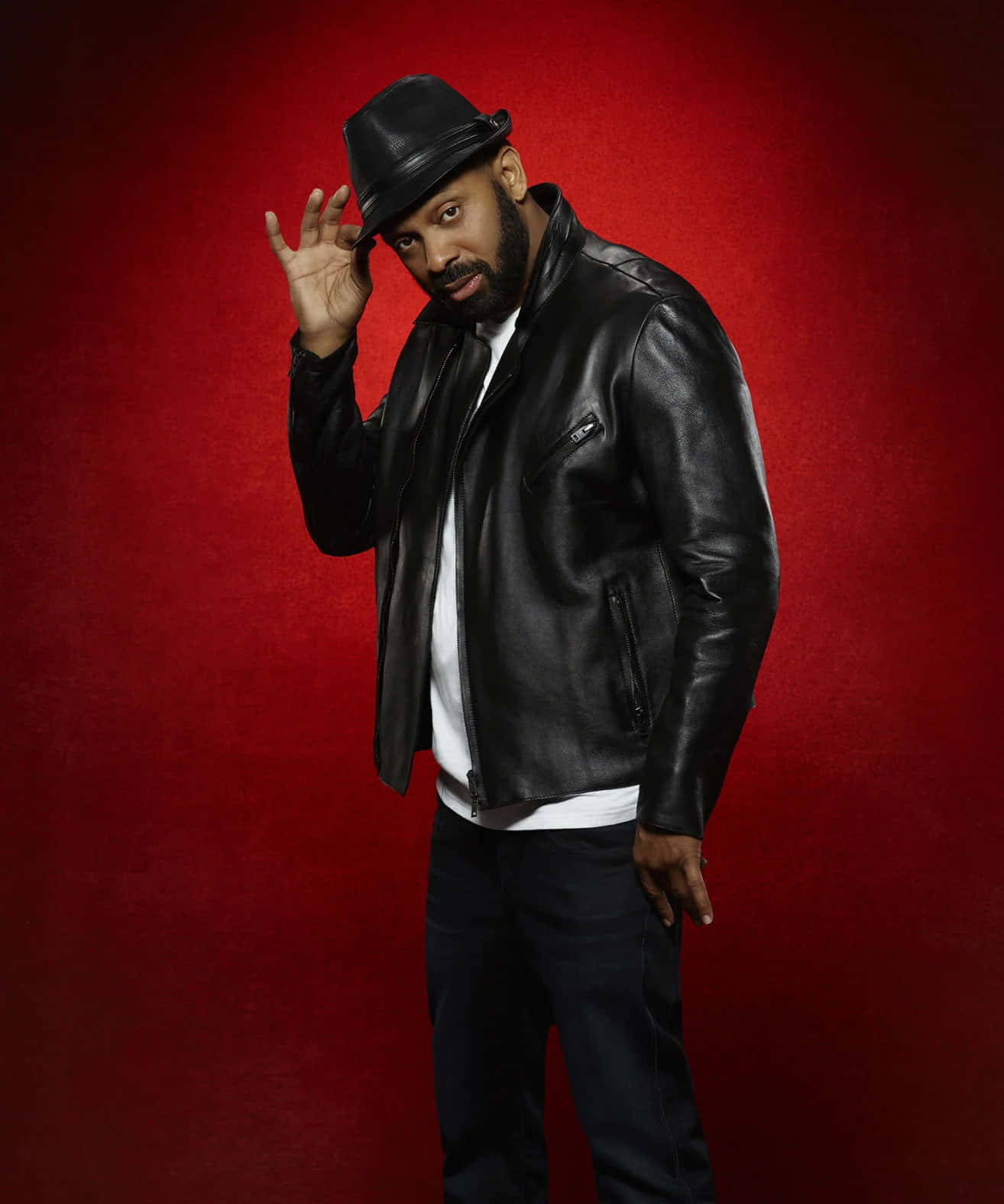 Mike Epps 桌布 壁紙 — 一位時尚男士身穿黑色皮褸和紳士帽，在豐富的紅色紋理背景前自信地擺姿勢。