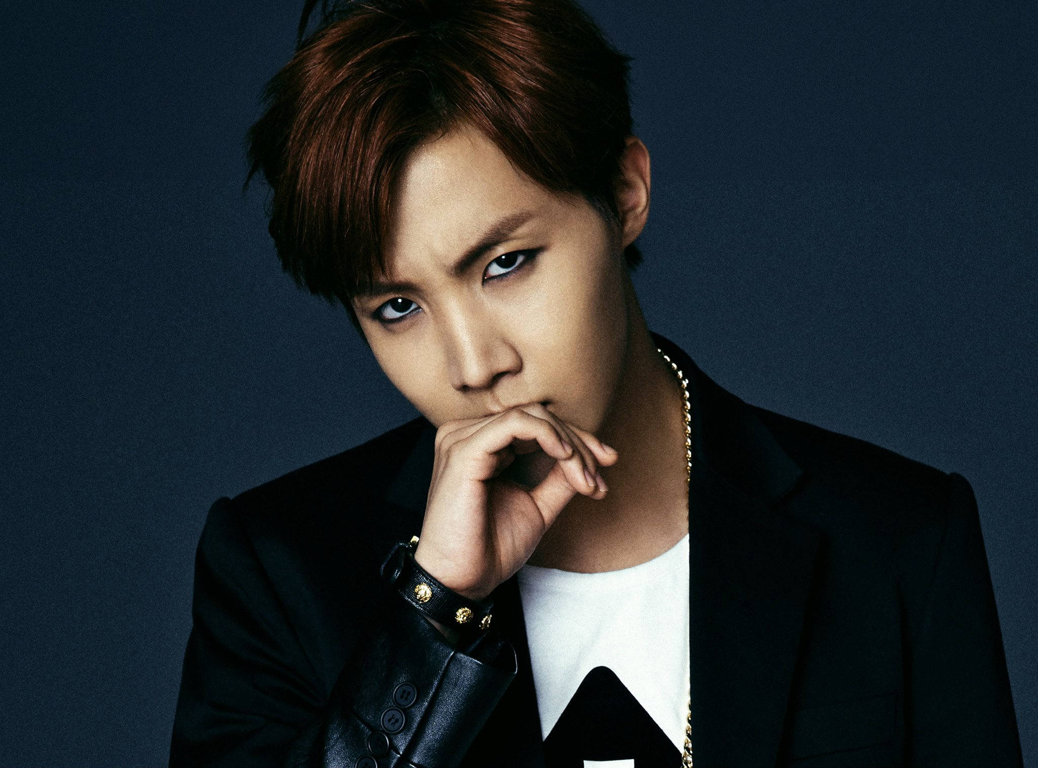 J-hope Dark & Wild 壁紙 — 一位時尚的年輕紅髮男子，眼神銳利，穿著黑色西裝外套和金鏈，在深藍色工作室背景前擺姿勢。