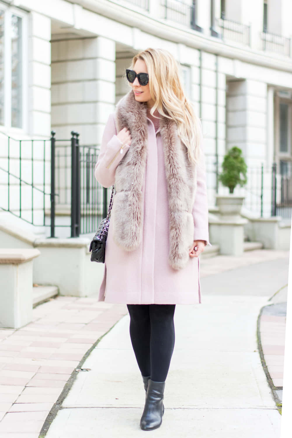 Pink Coat 桌布 壁紙 — 一位時尚的金髮女性穿著粉色外套和毛皮背心，戴著太陽眼鏡，手提包，自信地走在城市人行道上。