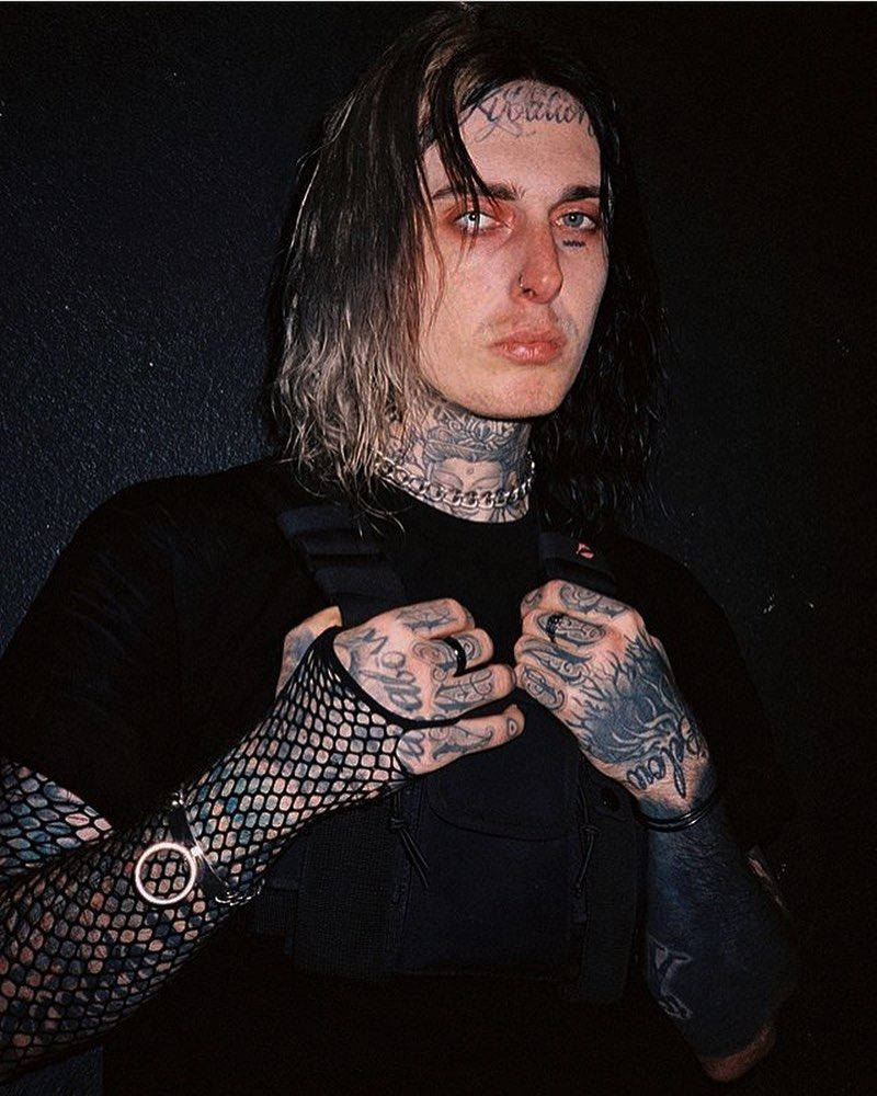 Ghostemane 桌布 壁紙 — 一位有紋身、長黑髮、戴魚網手套的人，穿著黑色背心在黑色背景前擺姿勢。