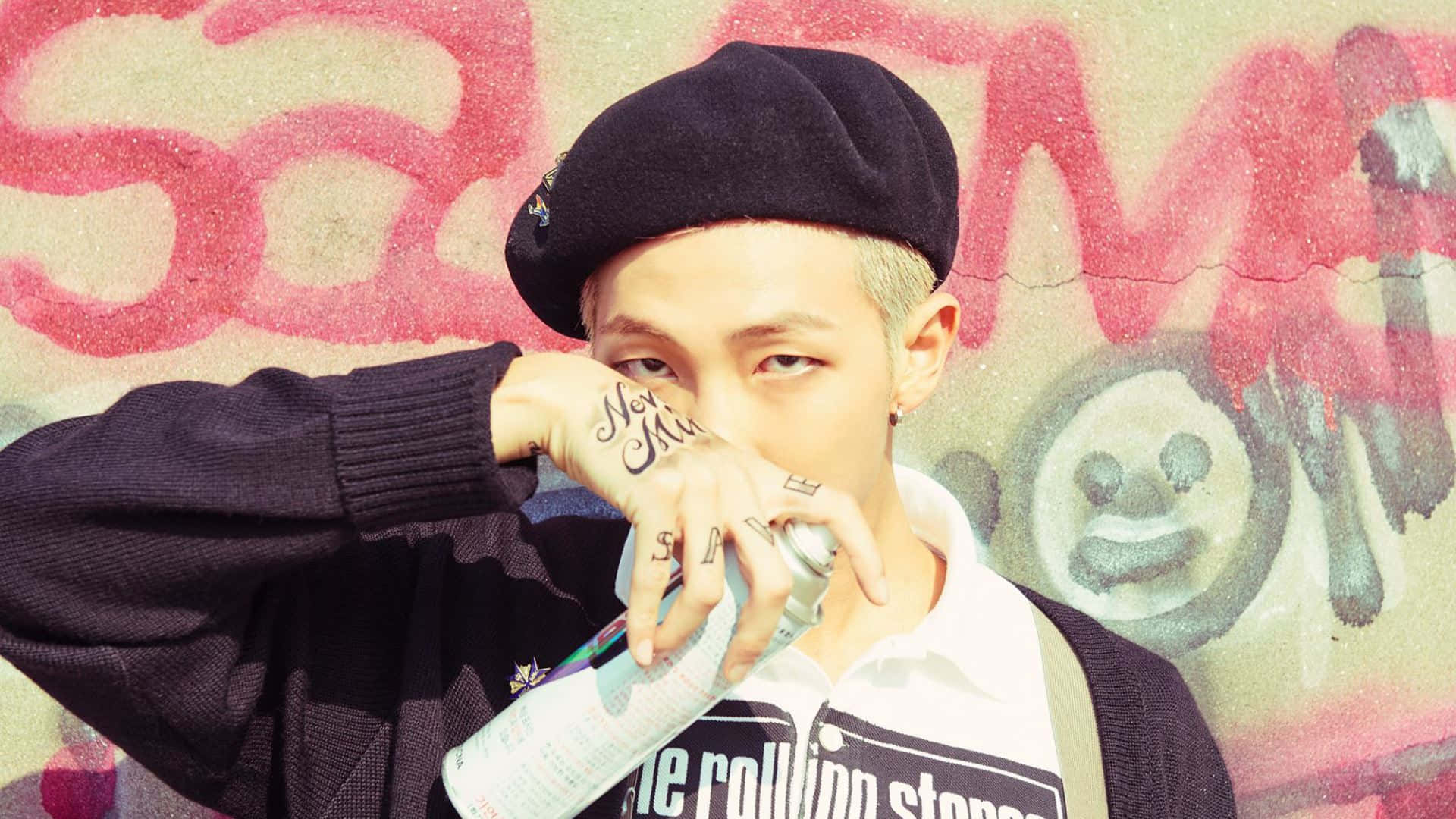 Bts Rap Monster 桌布 壁紙 — 一位有紋身並戴著貝雷帽的年輕人，在佈滿塗鴉的牆前拿著噴漆罐。