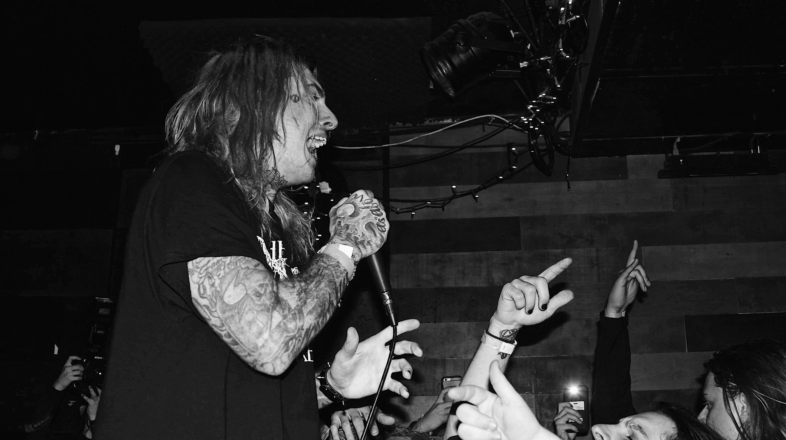 Ghostemane 桌布 壁紙 — 一位有紋身的音樂家在燈光昏暗的音樂會場地對著咪高峰尖叫，粉絲們伸手向上。