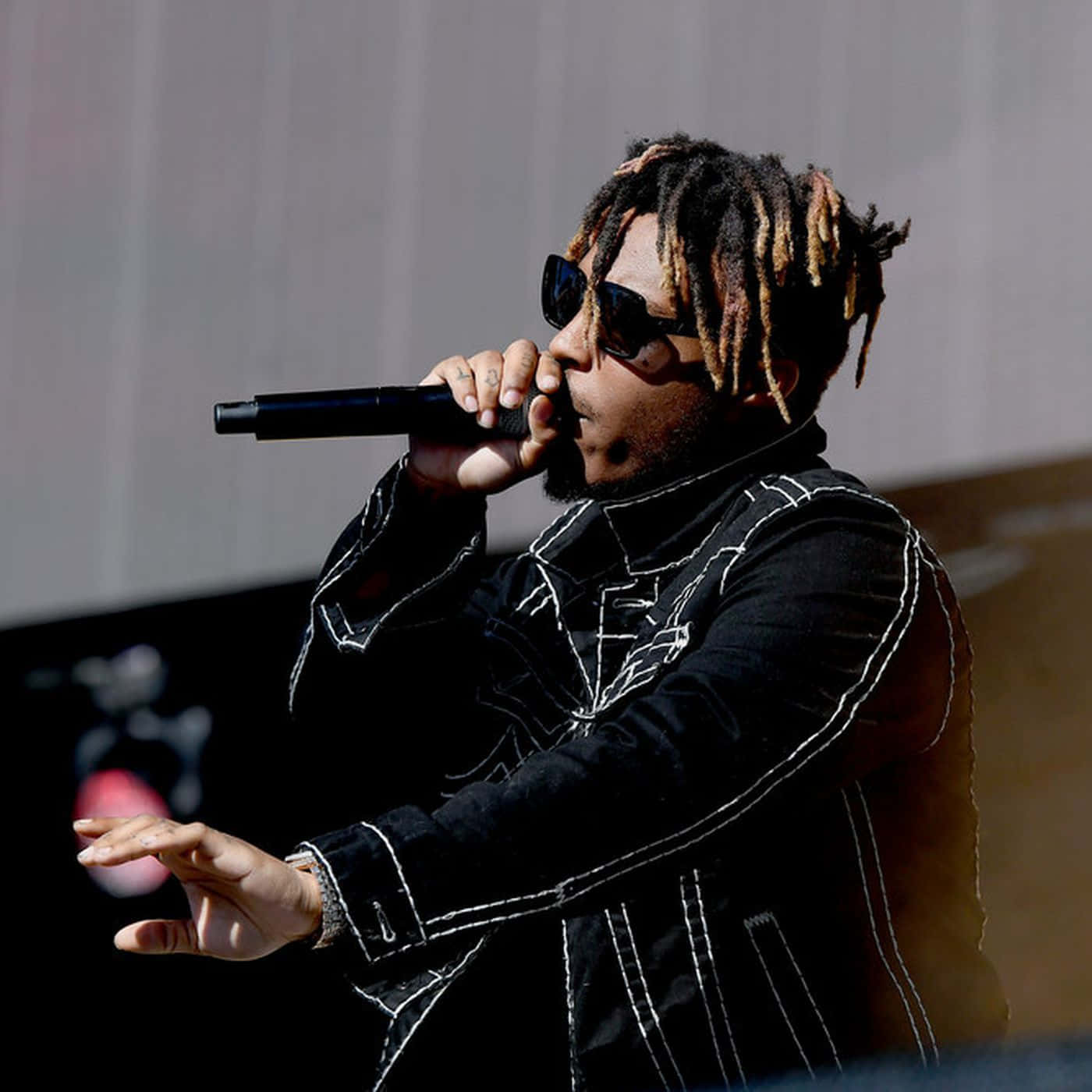 Dead Rappers Dreadlocks 壁紙 — 一位梳著辮子頭、戴著太陽眼鏡的饒舌歌手，在明亮的日光下於舞台上對著麥克風熱情表演。