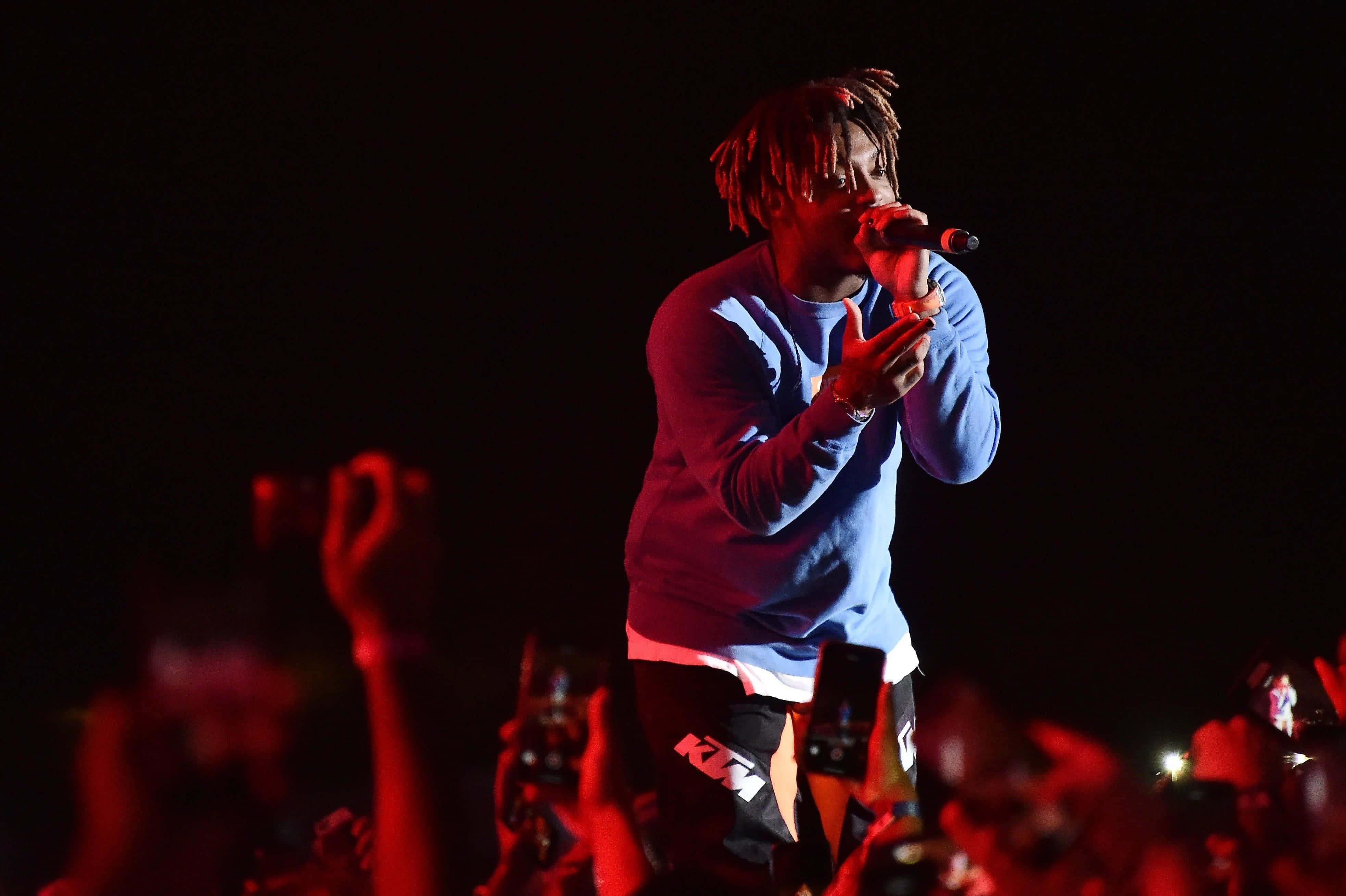 RIP Juice Wrld 壁紙 — 一位梳著辮子頭的饒舌歌手在紅色舞台燈光下對著麥克風唱歌，下方人群舉著手機。