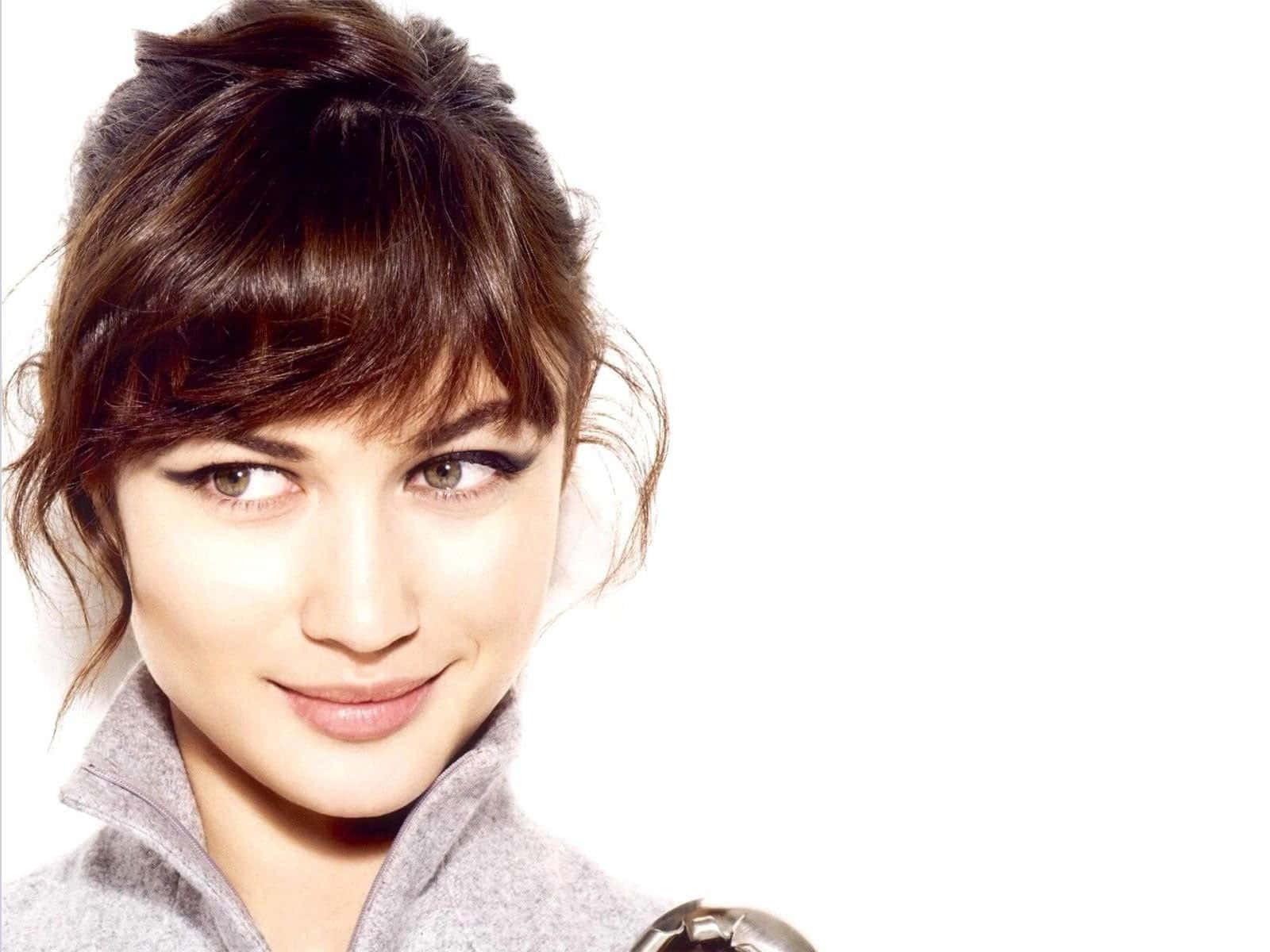 Olga Kurylenko 桌布 壁紙 — 一位棕色頭髮、畫著大膽眼線的女性，在純白背景前溫柔微笑的特寫肖像。