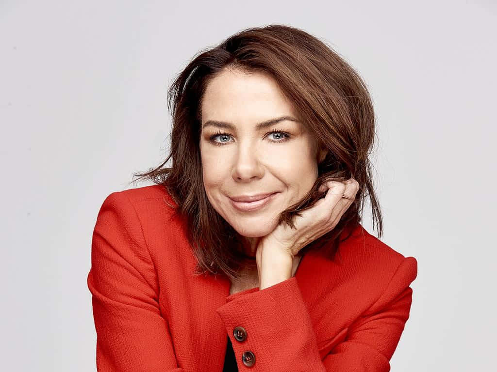 Kate Ritchie 桌布 壁紙 — 一位棕色頭髮、藍色眼睛的女性，在純白背景前穿著紅色西裝外套，將下巴靠在手上，溫柔地微笑。