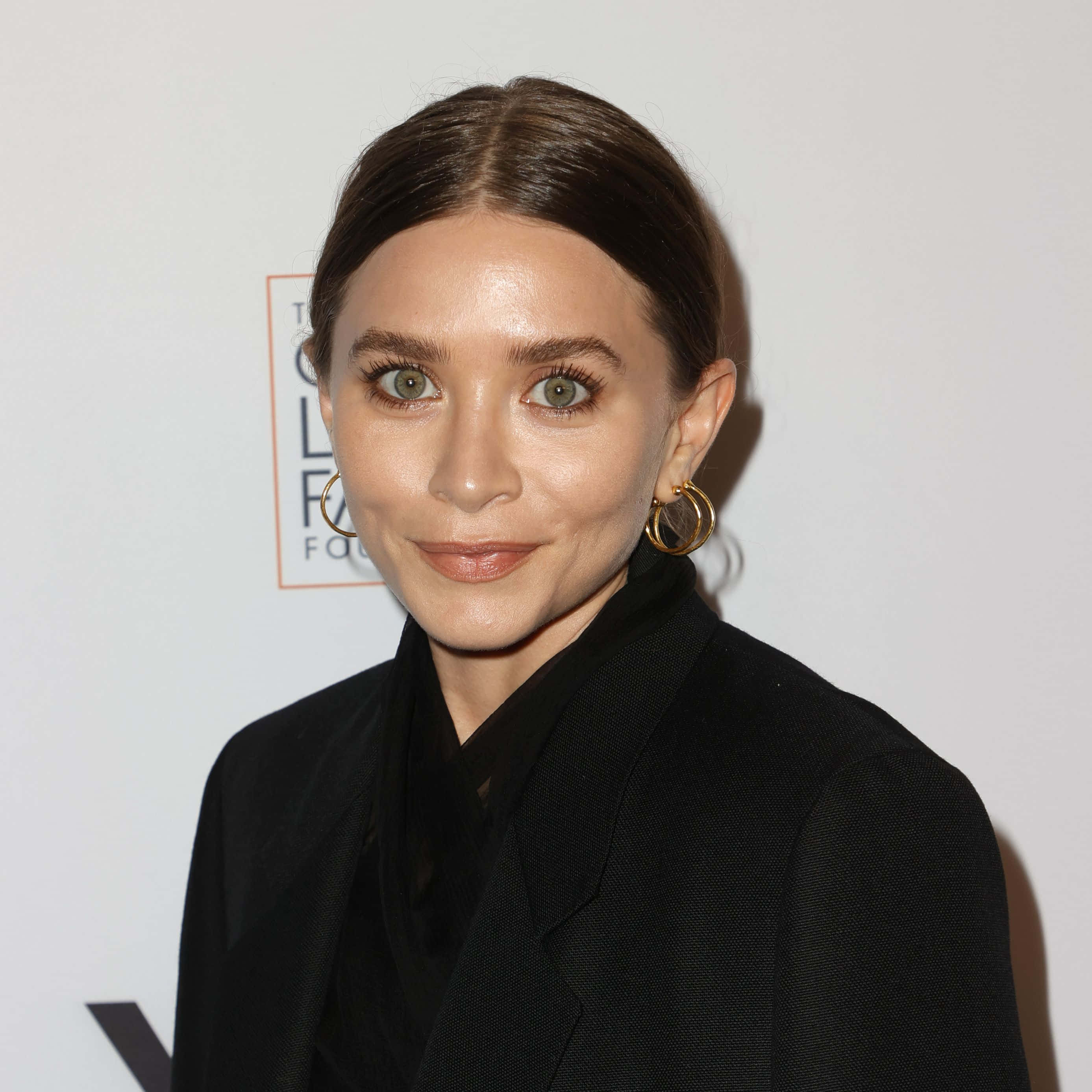ashley olsen 桌布 壁紙 — 一位棕色頭髮向後梳的女性在正式活動中穿著黑色西裝外套和金色耳環。