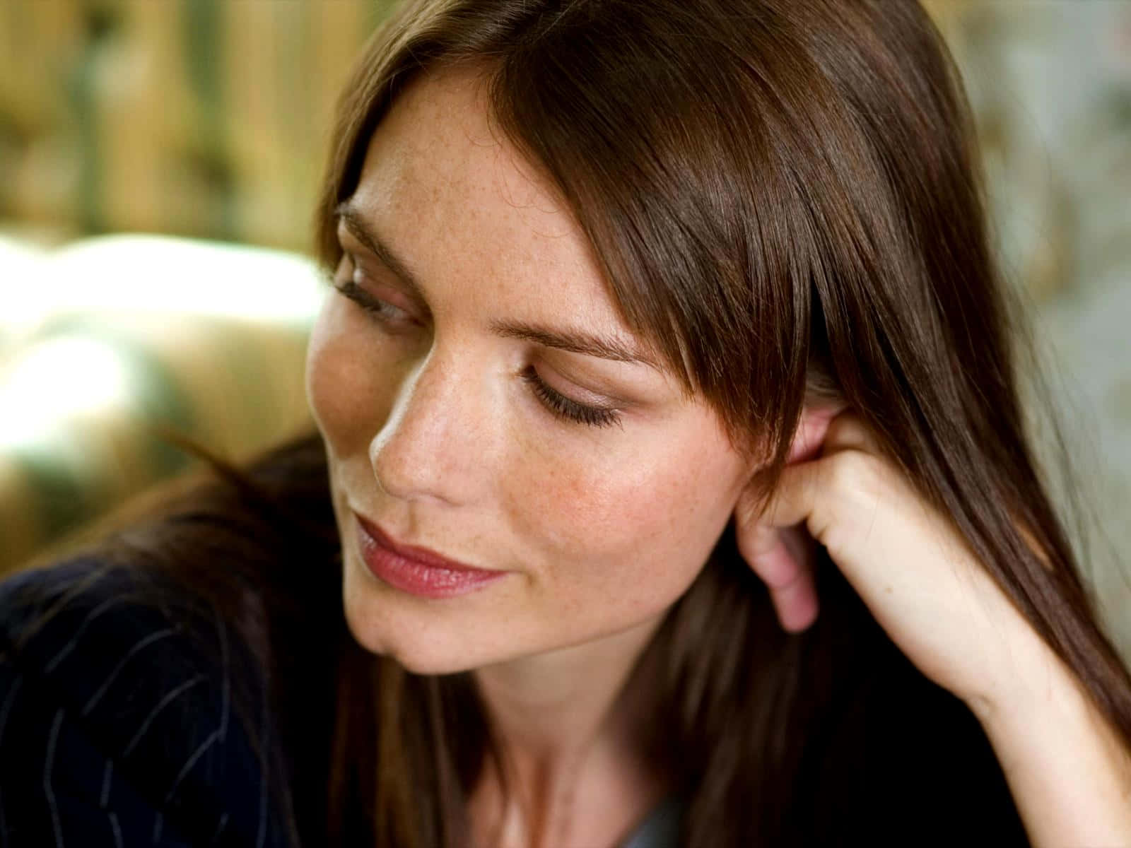 Saffron Burrows 桌布 壁紙 — 一位棕色頭髮的女性以柔和、沉思的姿勢將頭靠在手上。
