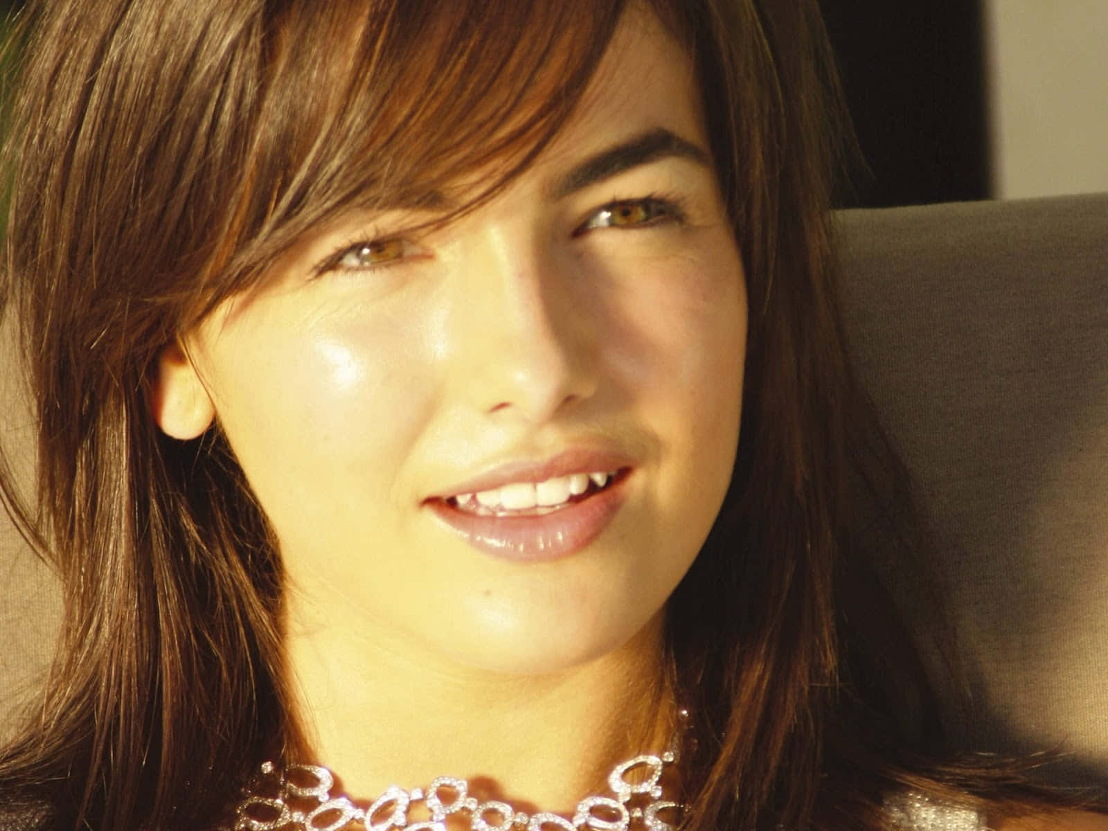 Camilla Belle 桌布 壁紙 — 一位棕色頭髮的女性在柔和的金色陽光中溫暖微笑的特寫肖像。