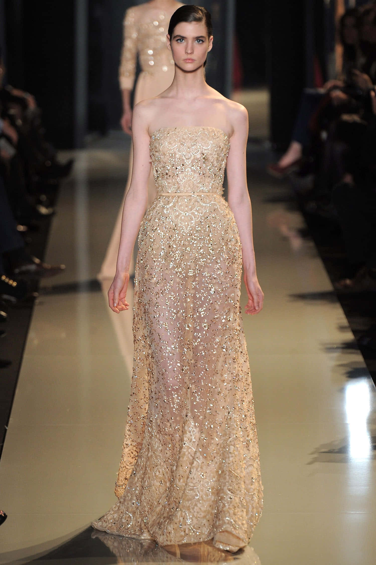 Beautiful Fashion 桌布 壁紙 — 一位模特兒在明亮的舞台燈光下，穿著優雅的金色亮片無肩帶長裙，自信地走在天橋上。