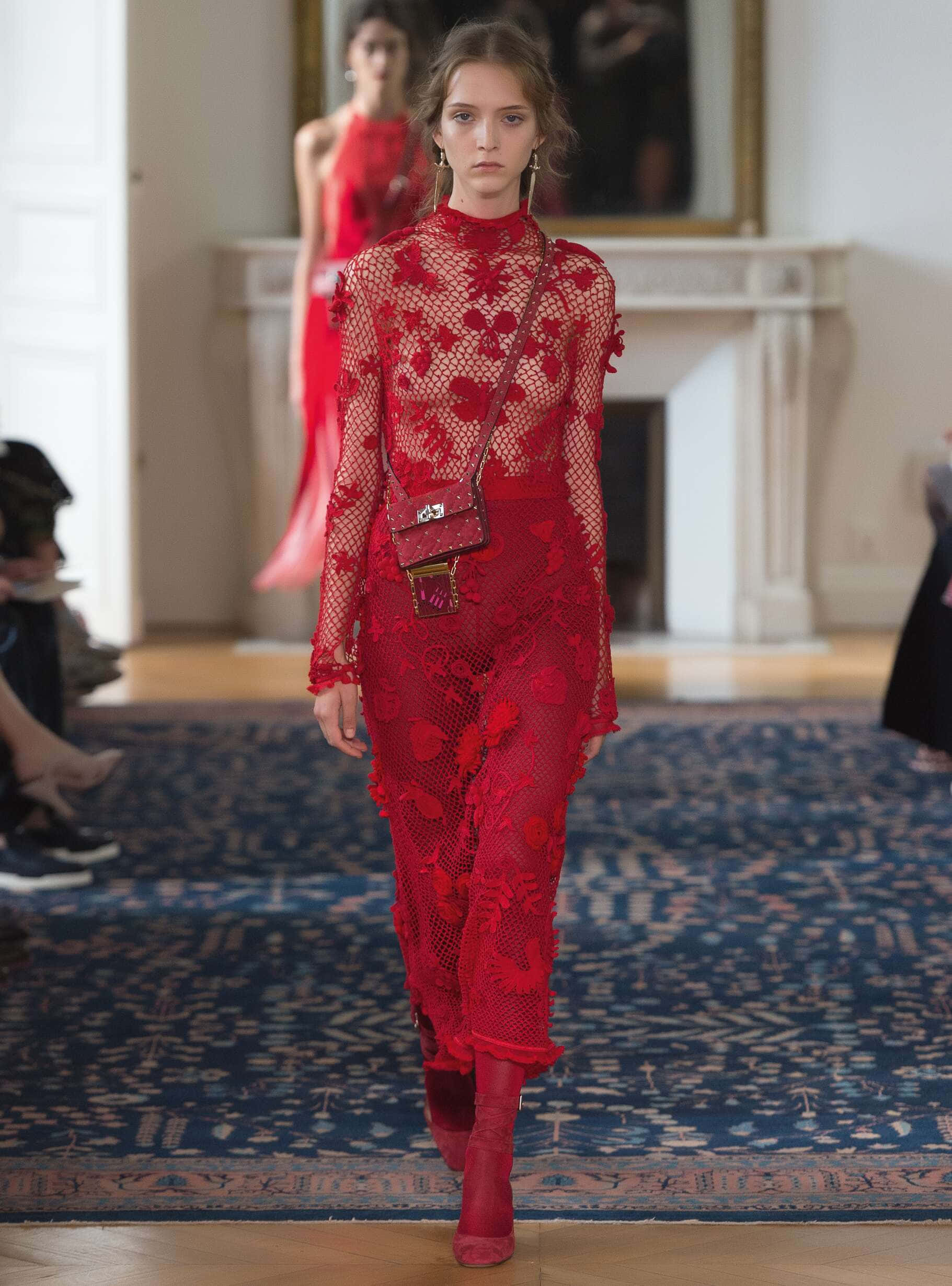 Fashion 桌布 壁紙 — 一位模特兒自信地穿著大膽的紅色蕾絲長袍，搭配相配的靴子和手袋，走在鋪有華麗藍色地毯和白色壁爐的跑道上。