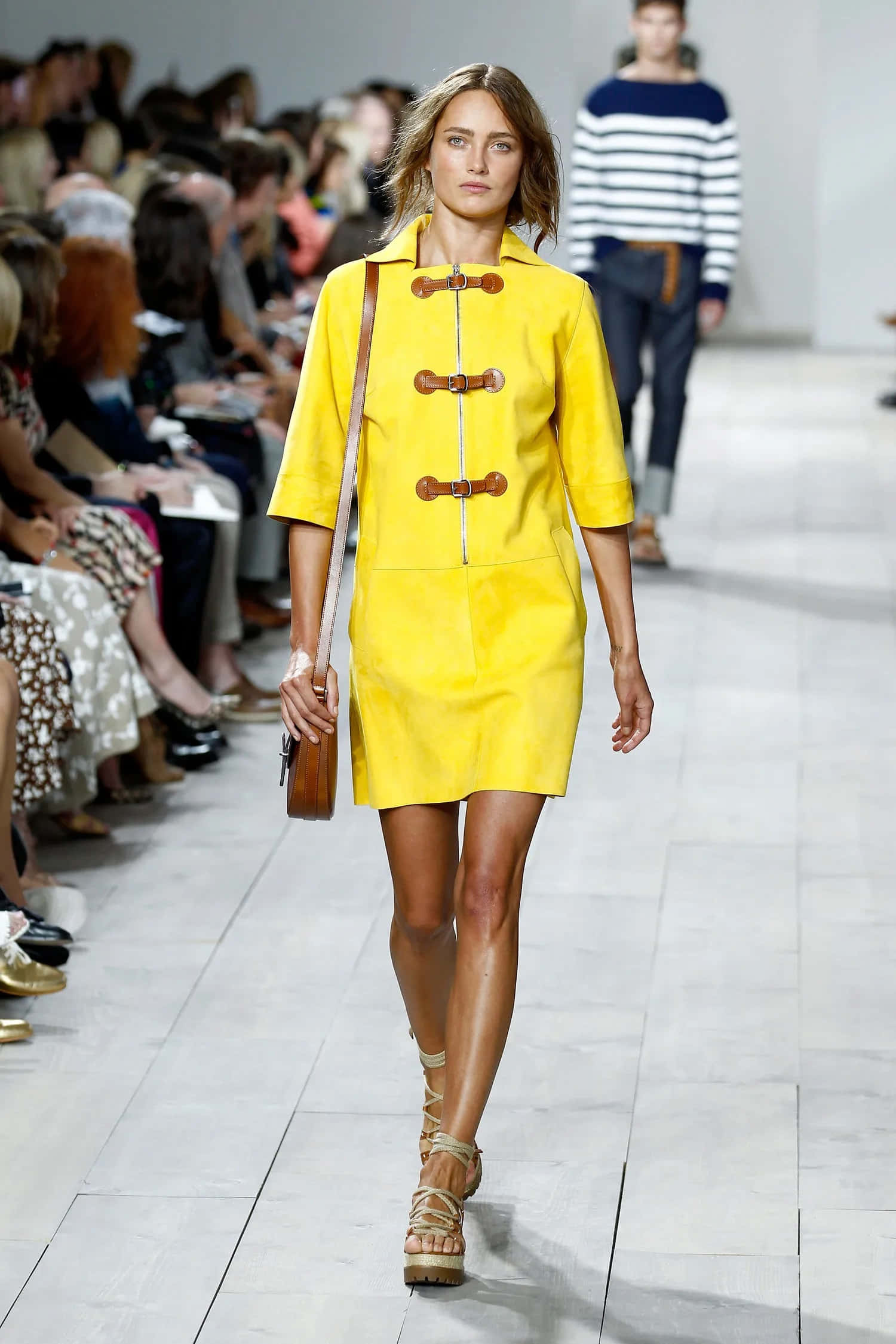Yellow Fashion 桌布 壁紙 — 一位模特兒自信地走在天橋上，身穿鮮黃色牛角扣大衣連衣裙，配以木質紐扣和棕褐色涼鞋。