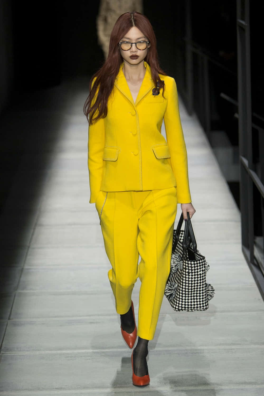 Yellow Fashion 桌布 壁紙 — 一位模特兒自信地走在天橋上，身穿大膽的黃色西裝，手持黑白格紋手袋。