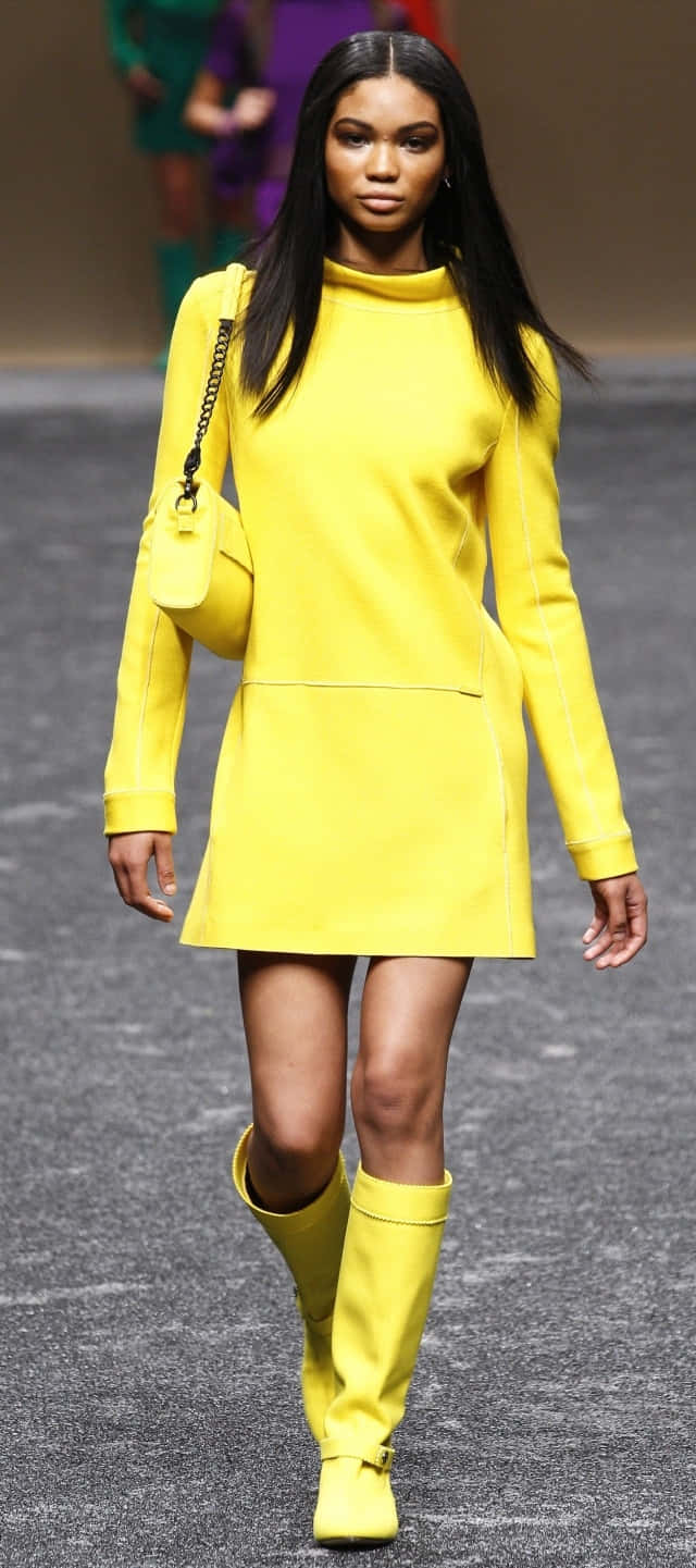 Yellow Fashion 桌布 壁紙 — 一位模特兒自信地走在天橋上，身穿大膽的黃色套裝，包括貼身連身裙、及大腿的靴子和相配的手袋。