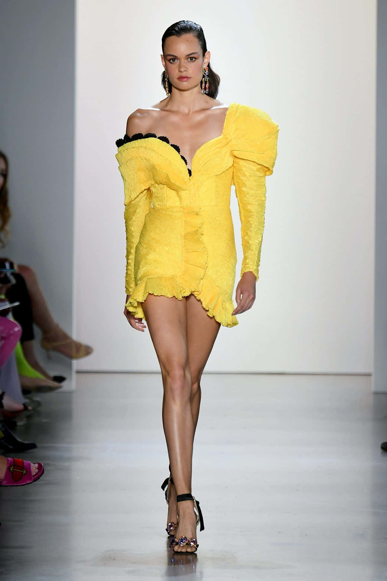 Yellow Fashion 桌布 壁紙 — 一位模特兒自信地走在天橋上，身穿大膽的黃色荷葉邊迷你裙，配以黑色飾邊和高跟鞋。