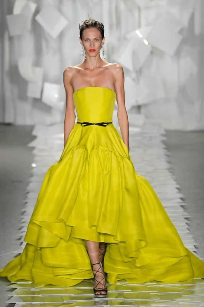 Yellow Fashion 桌布 壁紙 — 一位模特兒自信地走在天橋上，身穿鮮黃色無肩帶長裙，配以黑色腰帶和高低裙襬。