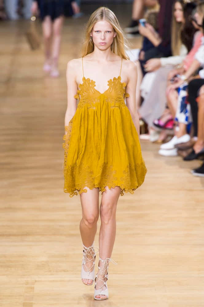 Yellow Fashion 桌布 壁紙 — 一位模特兒自信地走在木製天橋上，身穿芥末黃色蕾絲連衣裙和白色繫帶高跟鞋。