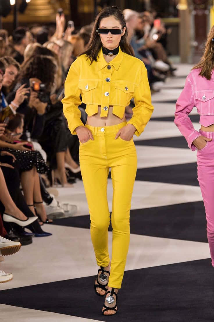 Yellow Fashion 桌布 壁紙 — 一位模特兒身穿大膽的黃色短身外套和配套長褲，自信地走在黑白條紋的T台上。