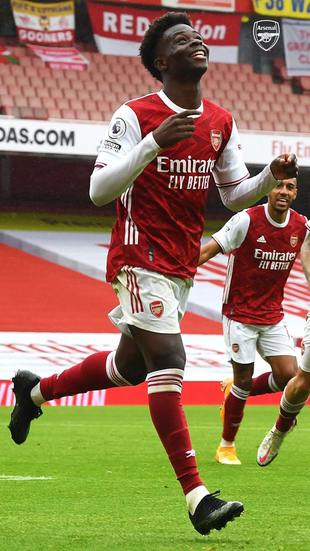 Arsenal 桌布 壁紙 — 一位欣喜若狂的阿仙奴足球員在充滿活力的綠色球場上跳躍慶祝，背景是體育場座位。