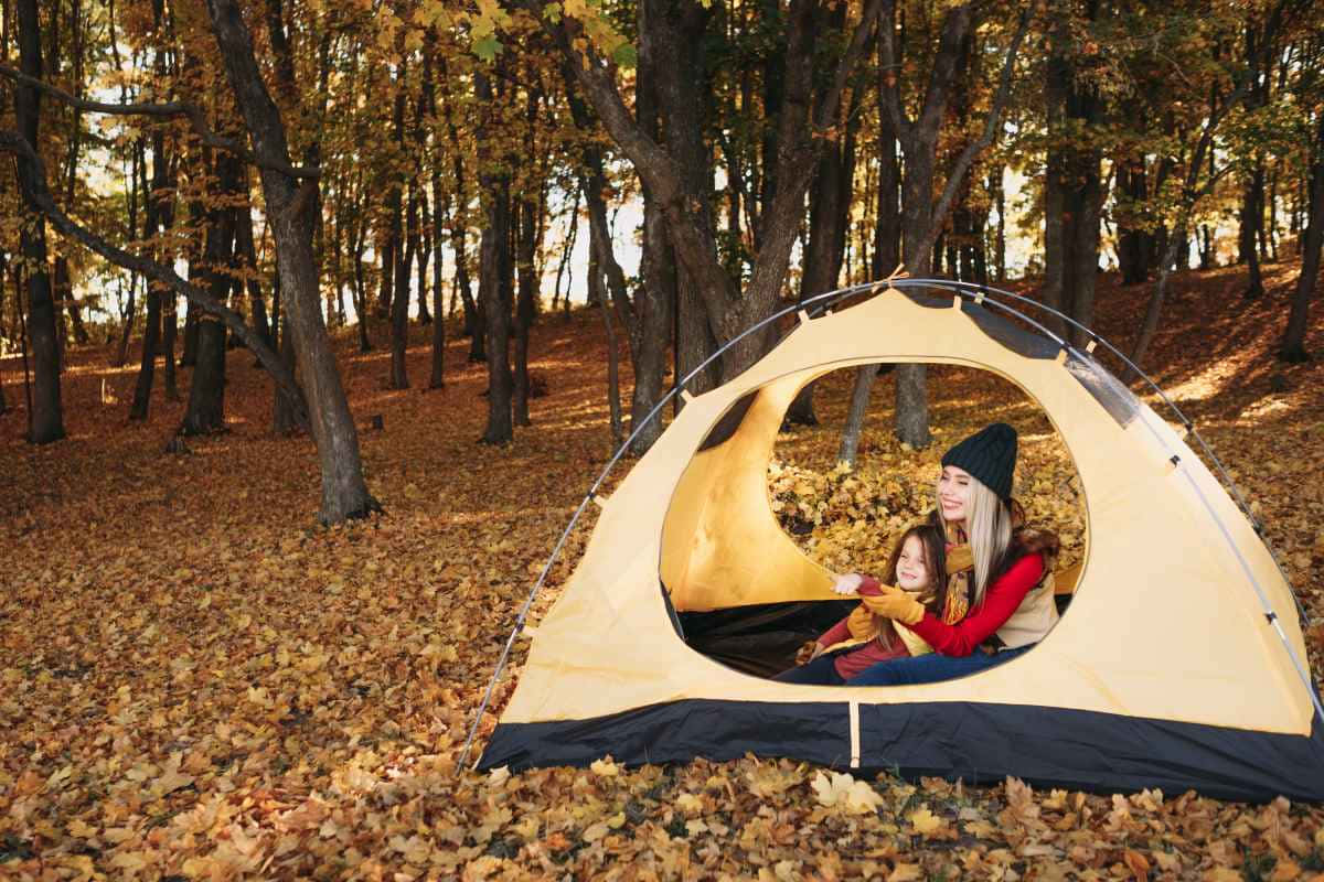 Fall Camping 桌布 壁紙 — 一位母親和女兒在一個被金色秋葉覆蓋的森林中的米色帳篷內溫暖地微笑。