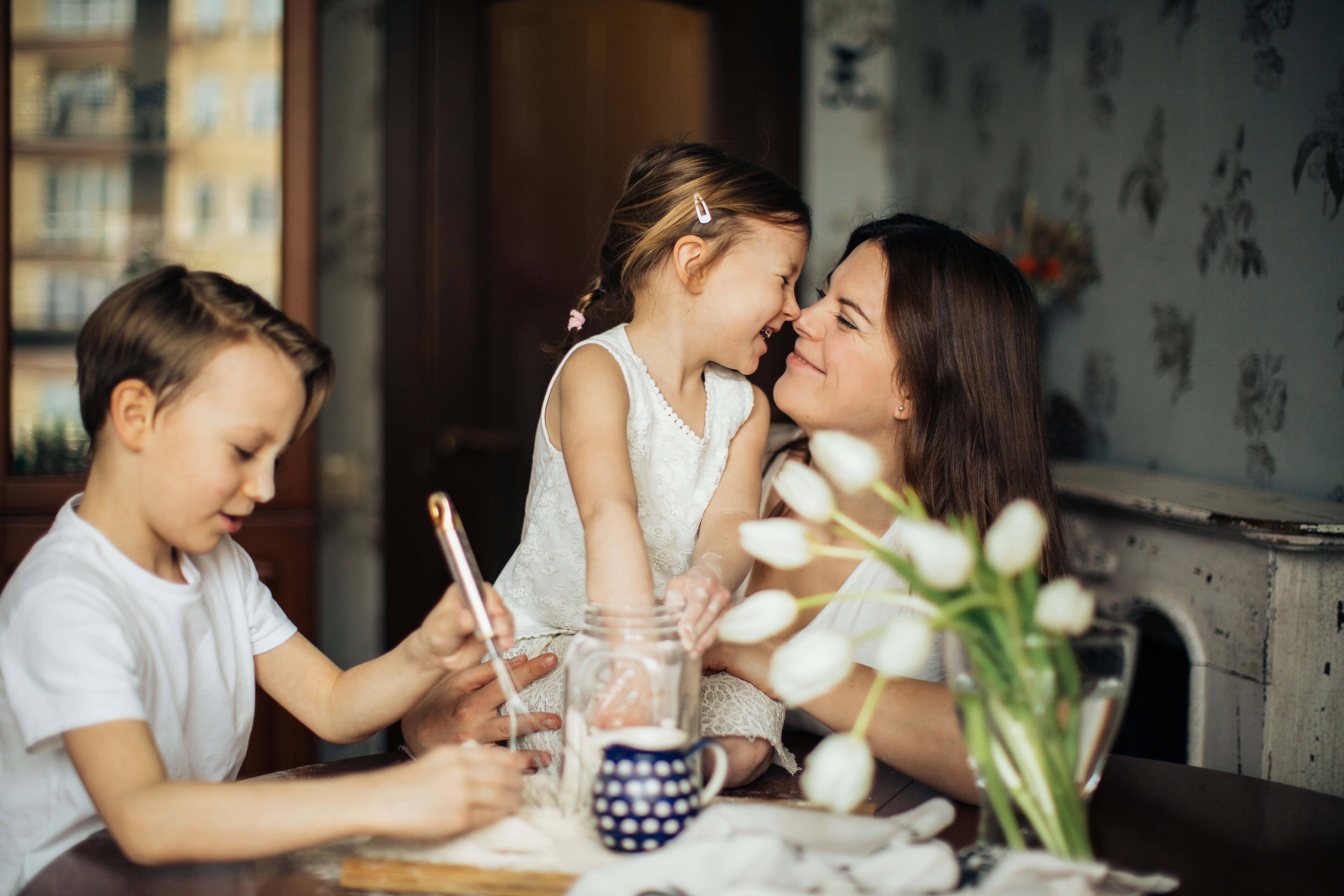 Mom 桌布 壁紙 — 一位母親和她的兩個孩子在擺有白色鬱金香和圓點馬克杯的餐桌上分享溫馨時刻。