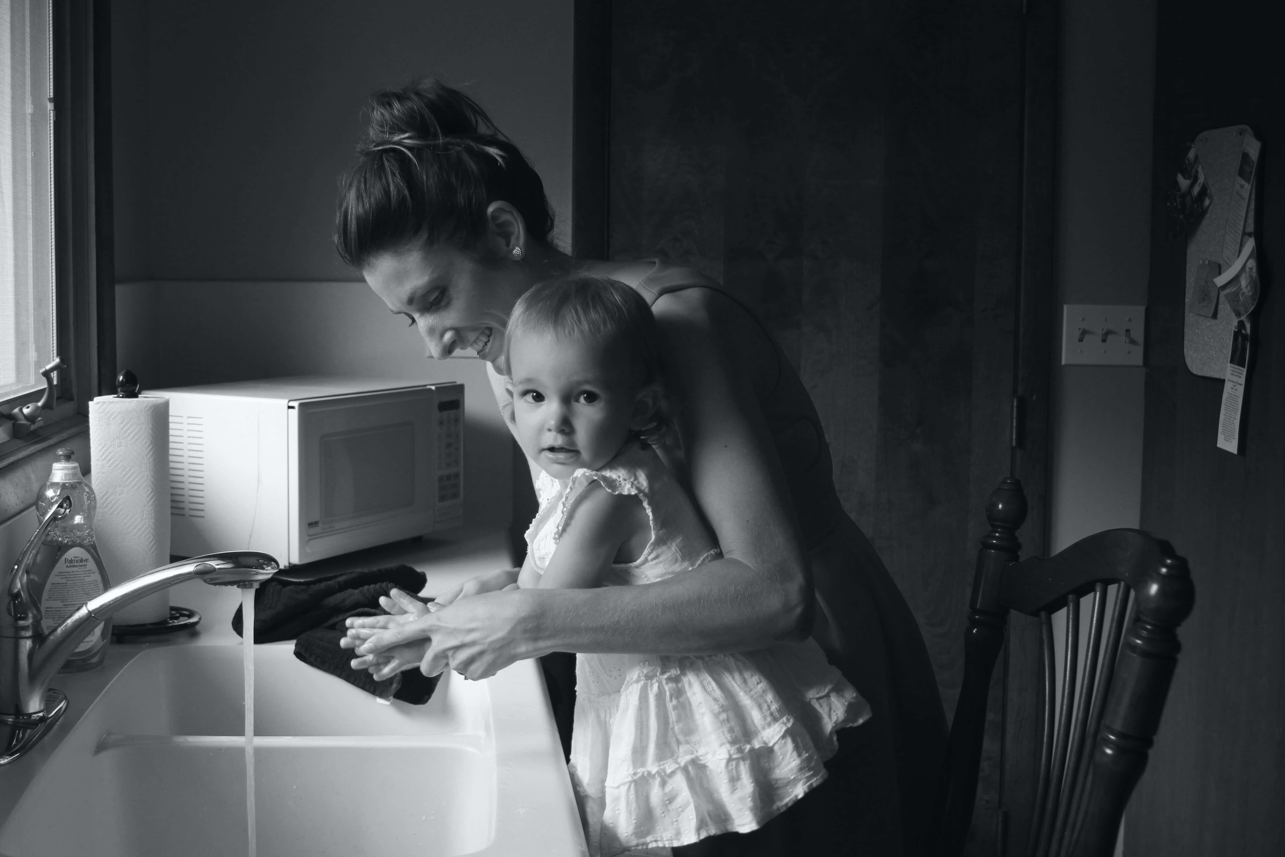Mom 桌布 壁紙 — 一位母親溫柔地引導她的幼兒在廚房水槽洗手，一個溫馨的黑白時刻。
